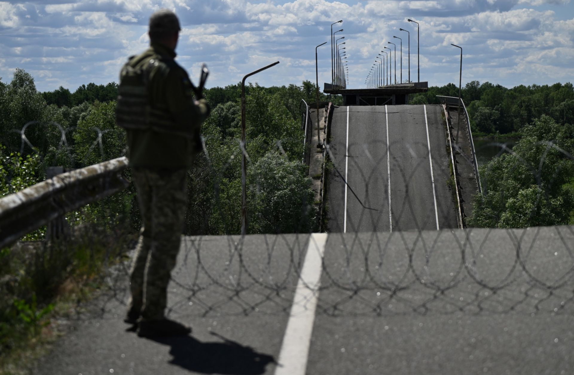 An officer of the State Border Guard Service of Ukraine stands on a destroyed bridge over the Dnipro River, which forms the state border between Ukraine and Belarus, on June 1, 2026.