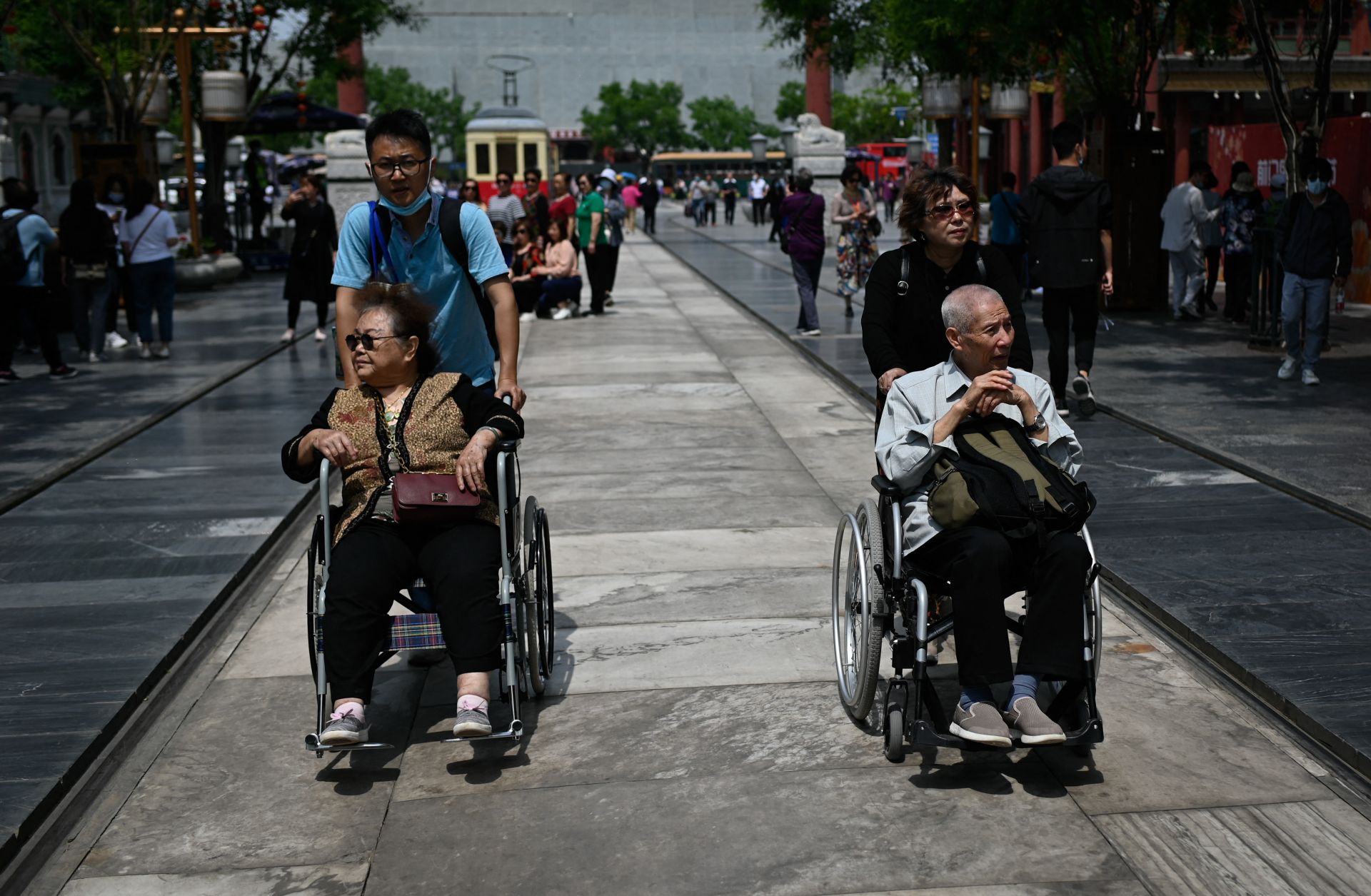 An elderly man and woman are pushed in wheelchairs along a street in Beijing, China, on May 11, 2021.