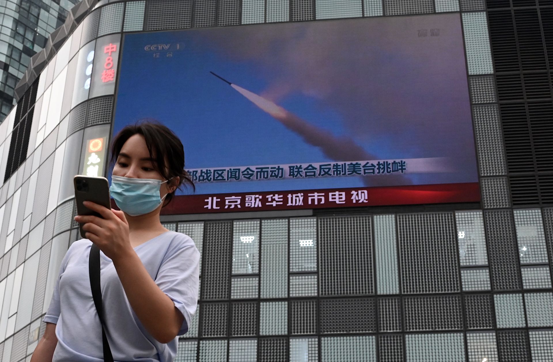 A woman in Beijing uses her mobile phone as she walks in front of a large screen showing a news broadcast about China's military exercises encircling Taiwan on Aug. 4.