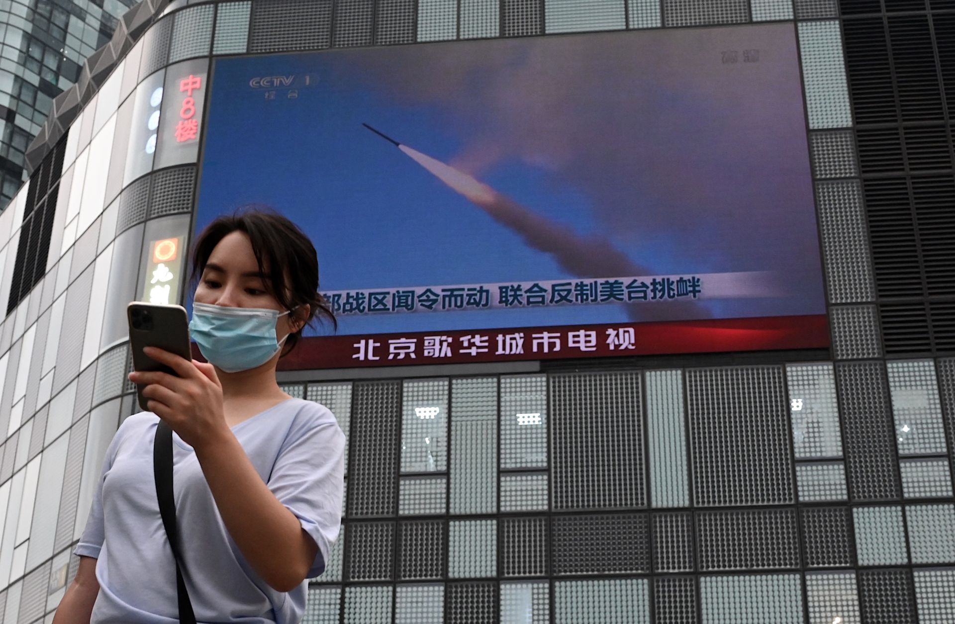 A woman in Beijing uses her mobile phone as she walks in front of a large screen showing a news broadcast about China's military exercises encircling Taiwan on Aug. 4. A woman in Beijing uses her mobile phone as she walks in front of a large screen showing a news broadcast about China's military exercises encircling Taiwan on Aug. 4.