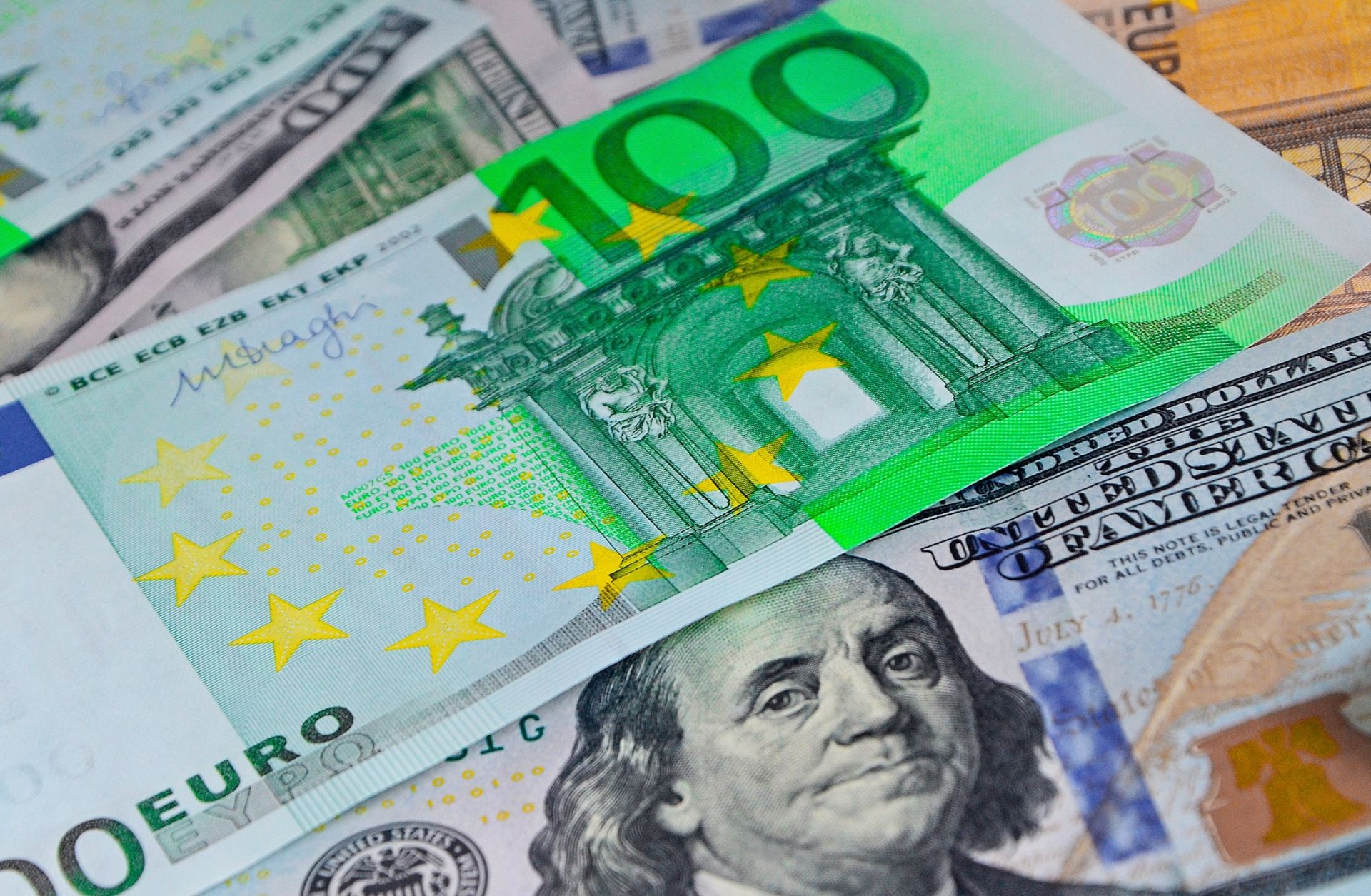Euro banknotes lie atop U.S. dollar banknotes.