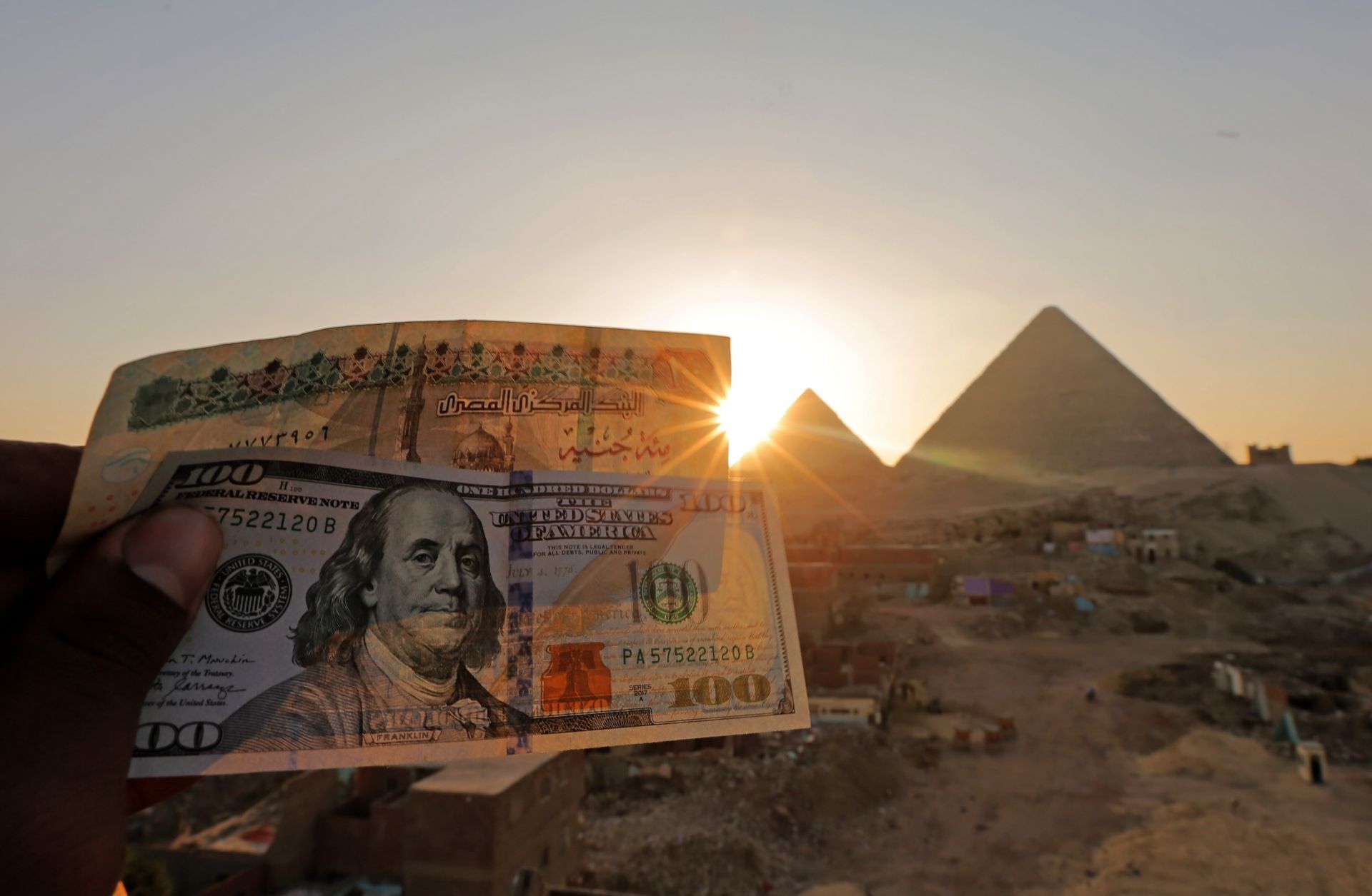 A 100-pound Egyptian banknote is held next to a $100 U.S. banknote near the Great Pyramids at Giza on Jan. 17, 2023.