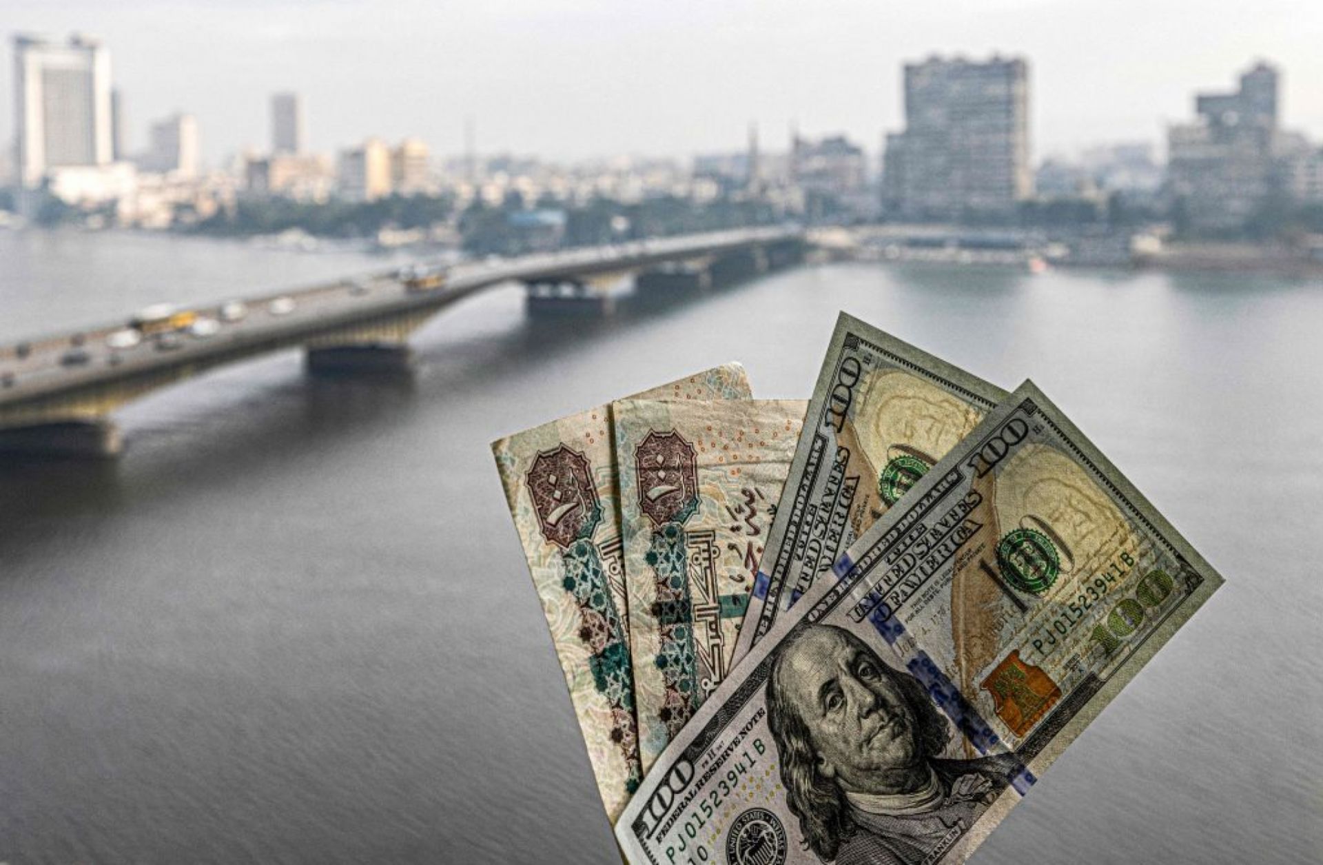 Two pairs of U.S. hundred dollar bills and Egyptian hundred pound notes are held before a window showing the skyline of Egypt's capital Cairo and the Nile River on Jan. 16, 2023.