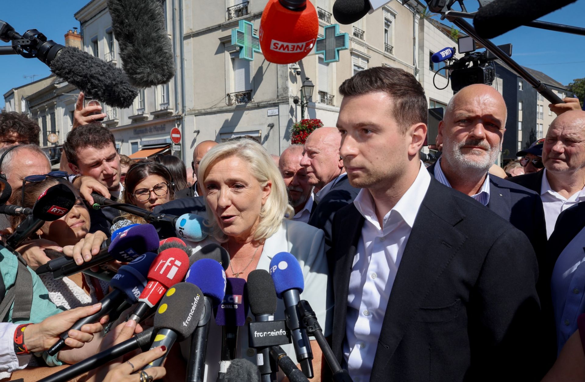 Journalists surround French far-right National Rally leader Marine Le Pen (center) as she arrives with National Rally president Jordan Bardella (third from right) for a campaign rally in La Fleche, France, on July 8, 2026.