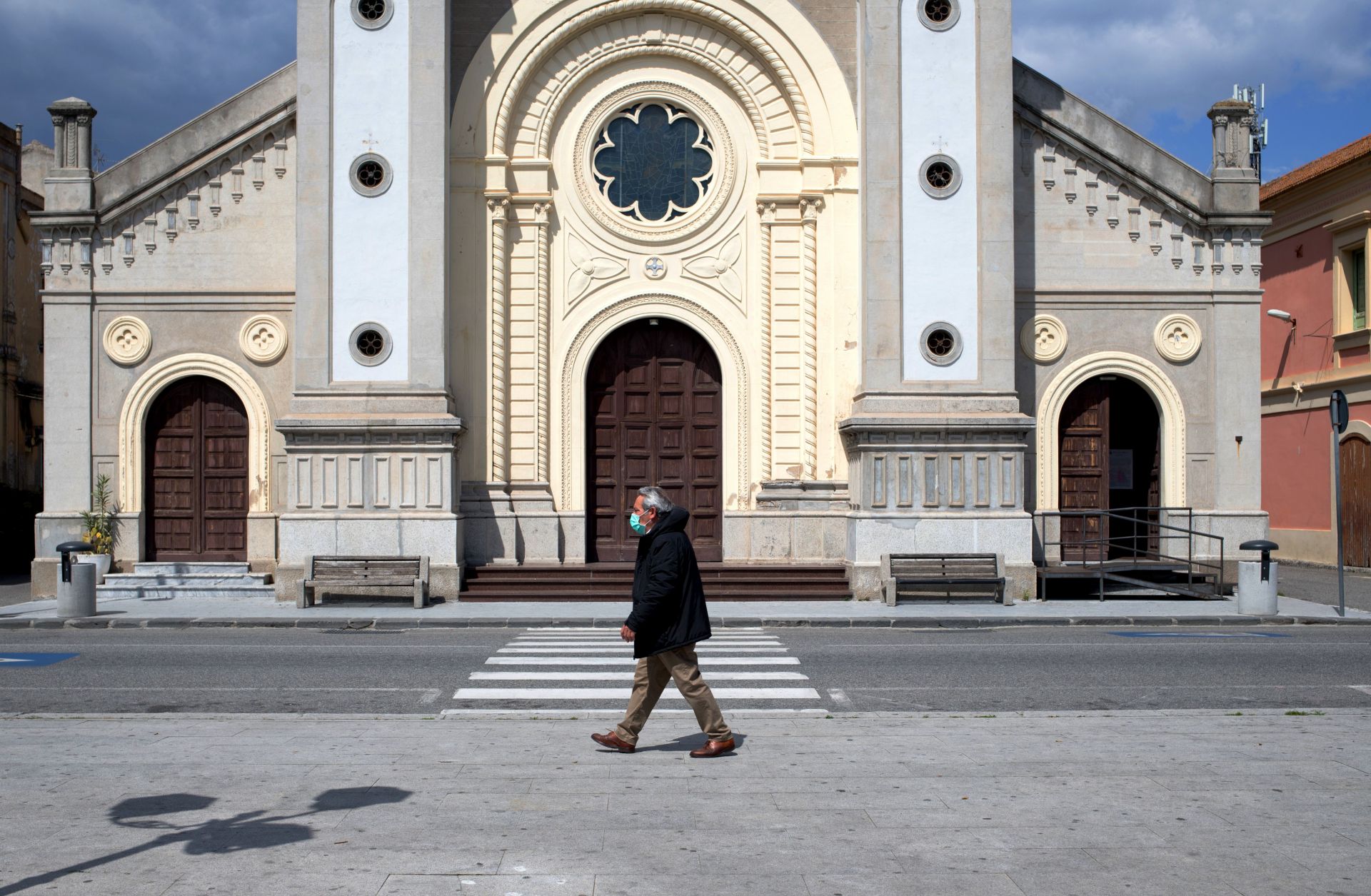 A man wearing a protective mask walks in the empty square in front of a cathedral in Locri, Italy, on April 7, 2020. 