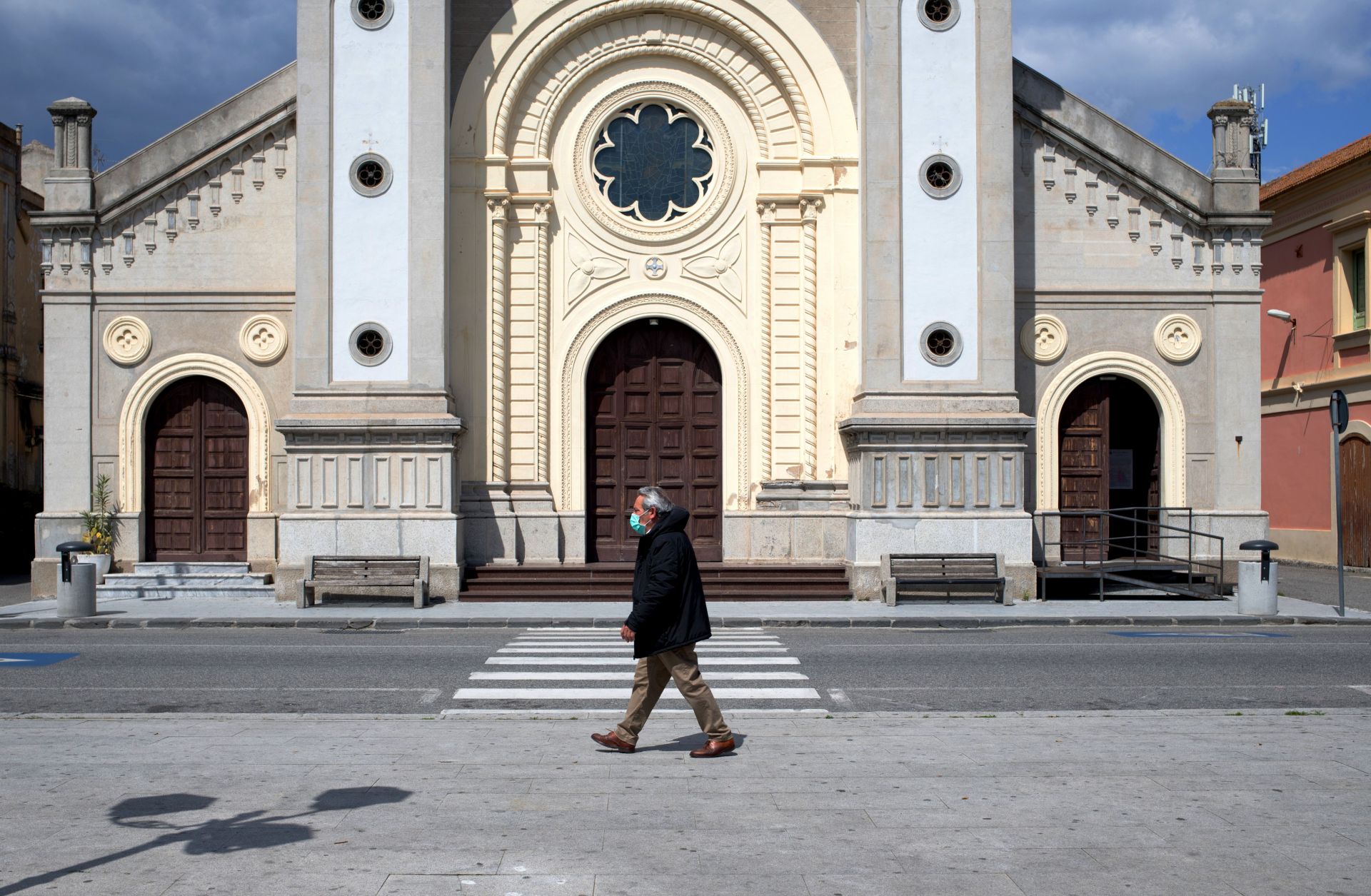 A man wearing a protective mask in Locri, Italy. A man wearing a protective mask walks in the empty square in front of a cathedral in Locri, Italy, on April 7, 2020.