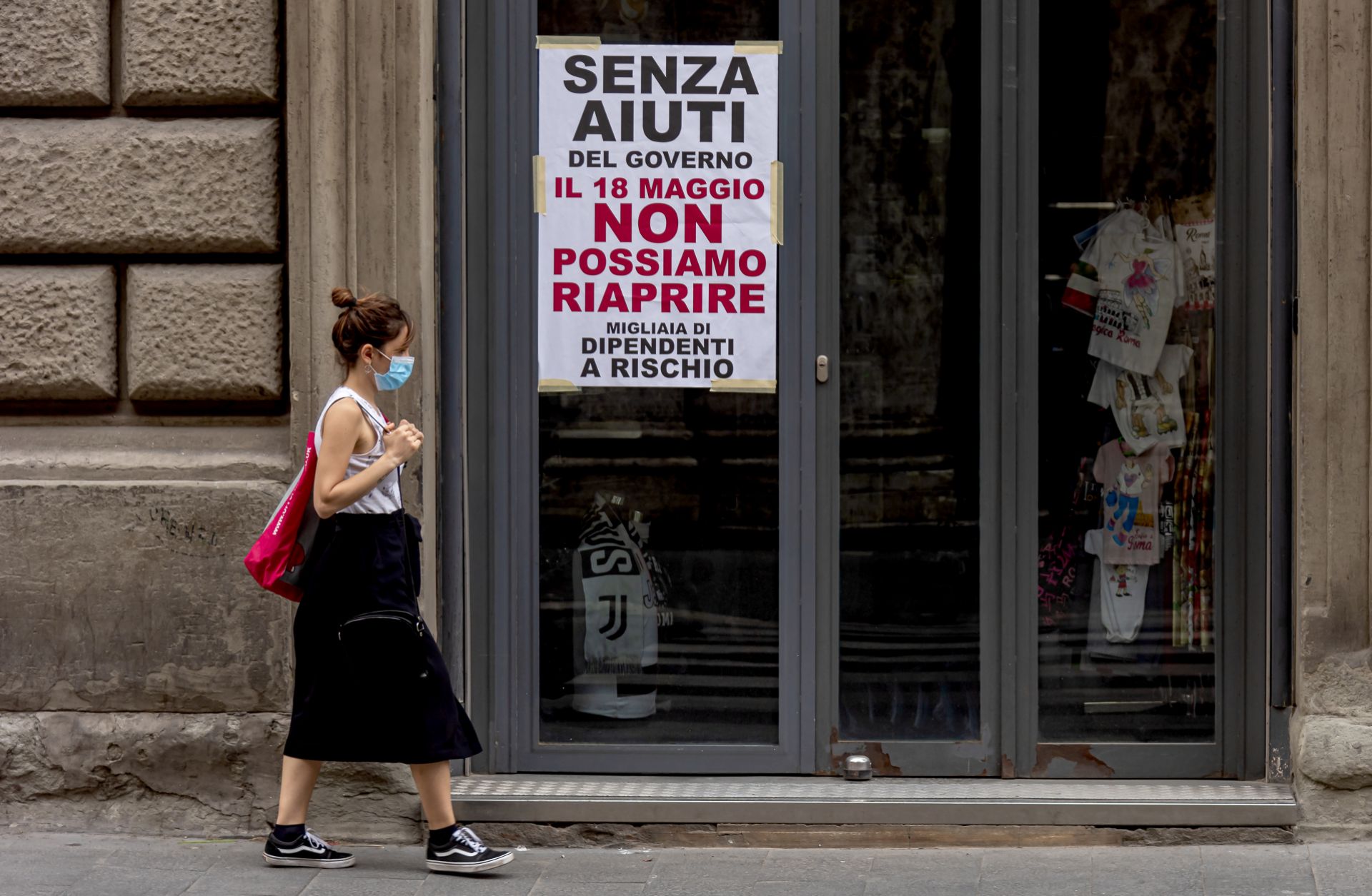 A woman wearing a face mask walks past a closed shop in Rome, Italy, on May 18, 2020. The sign on the store window reads "Without government aid, we cannot reopen on May 18. Thousands of employees at risk." 