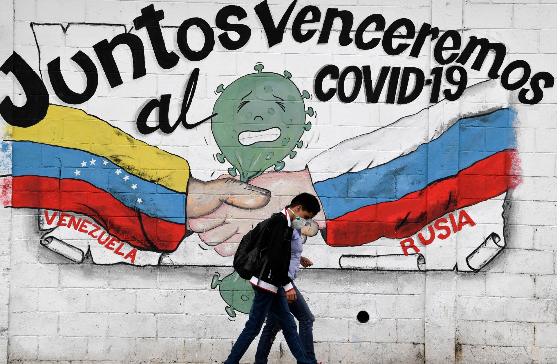 People walk past a mural of the Venezuelan and Russian flags that reads "Together we will defeat COVID-19" in Caracas, Venezuela, on March 4, 2021.