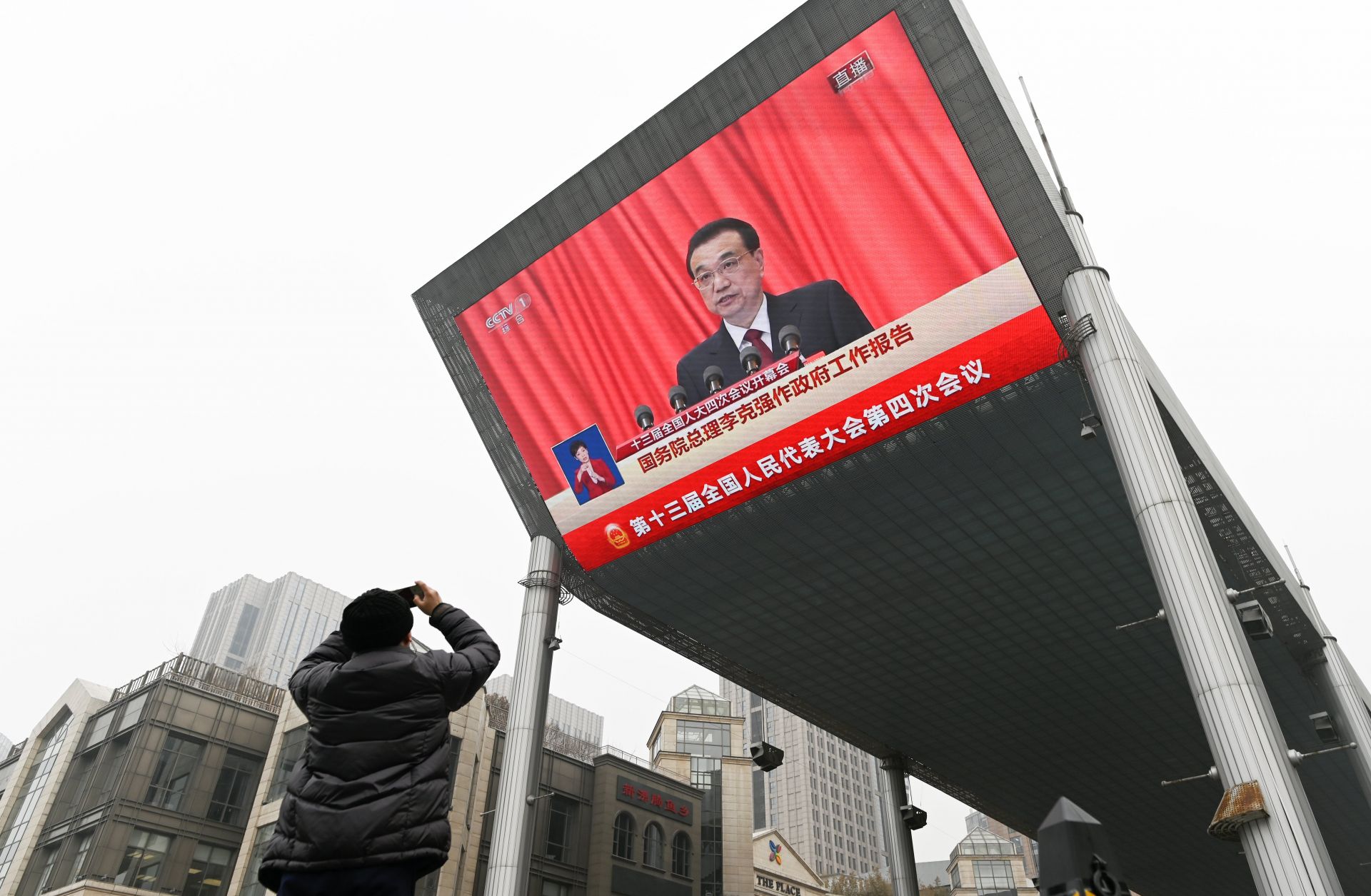 A man in Beijing, China, uses his mobile phone to take a picture of a big screen showing Chinese Premier Li Keqiang delivering a speech at the opening session of the National People's Congress (NPC) on March 5, 2021. 