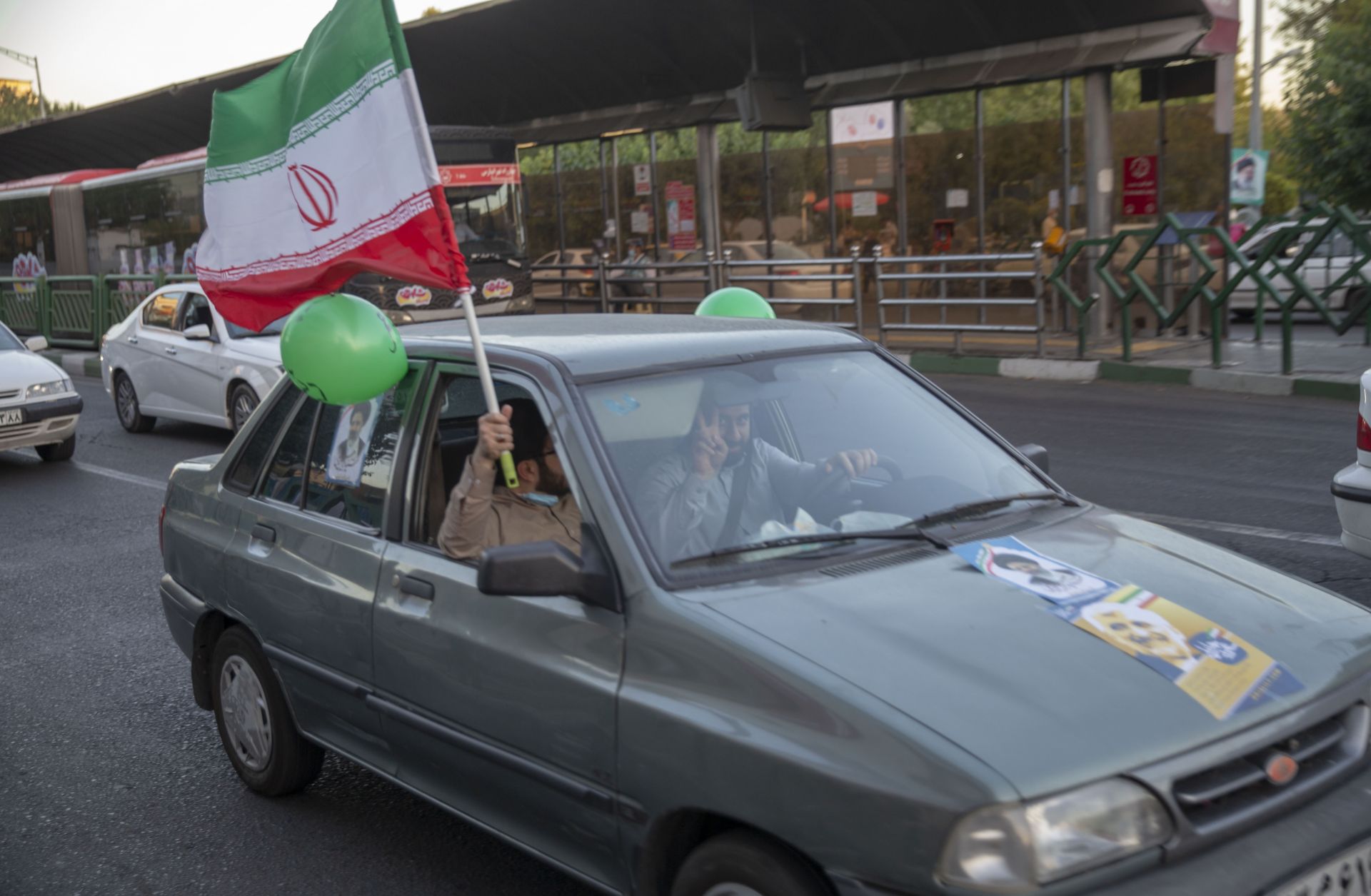 Supporters of Iranian presidential candidate Ebrahim Raisi hold an Iranian flag out of a car window on a street in Tehran on June 11, 2021. 
