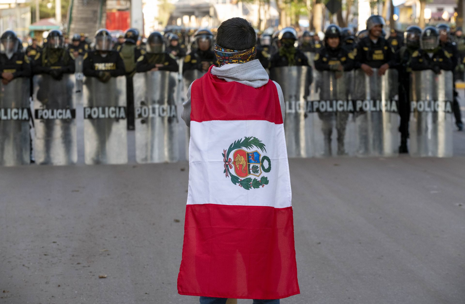 A demonstrator wearing the Peruvian flag stands in front of police officers forming a barrier with their riot shields near the entrance of the airport in Cusco, Peru, on Jan. 19, 2023.