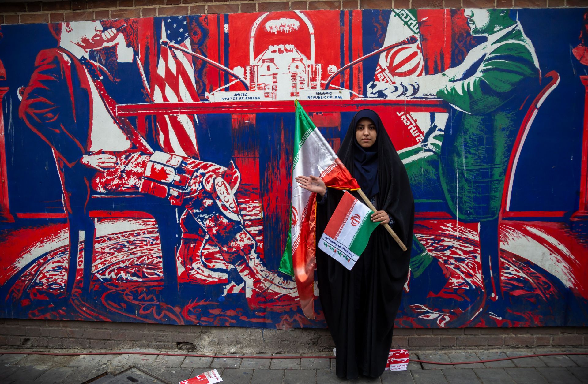 A woman holding an Iranian flag poses in front of an anti-U.S. mural on a wall of the former U.S. embassy in Tehran, Iran, on Nov. 4, 2023. 