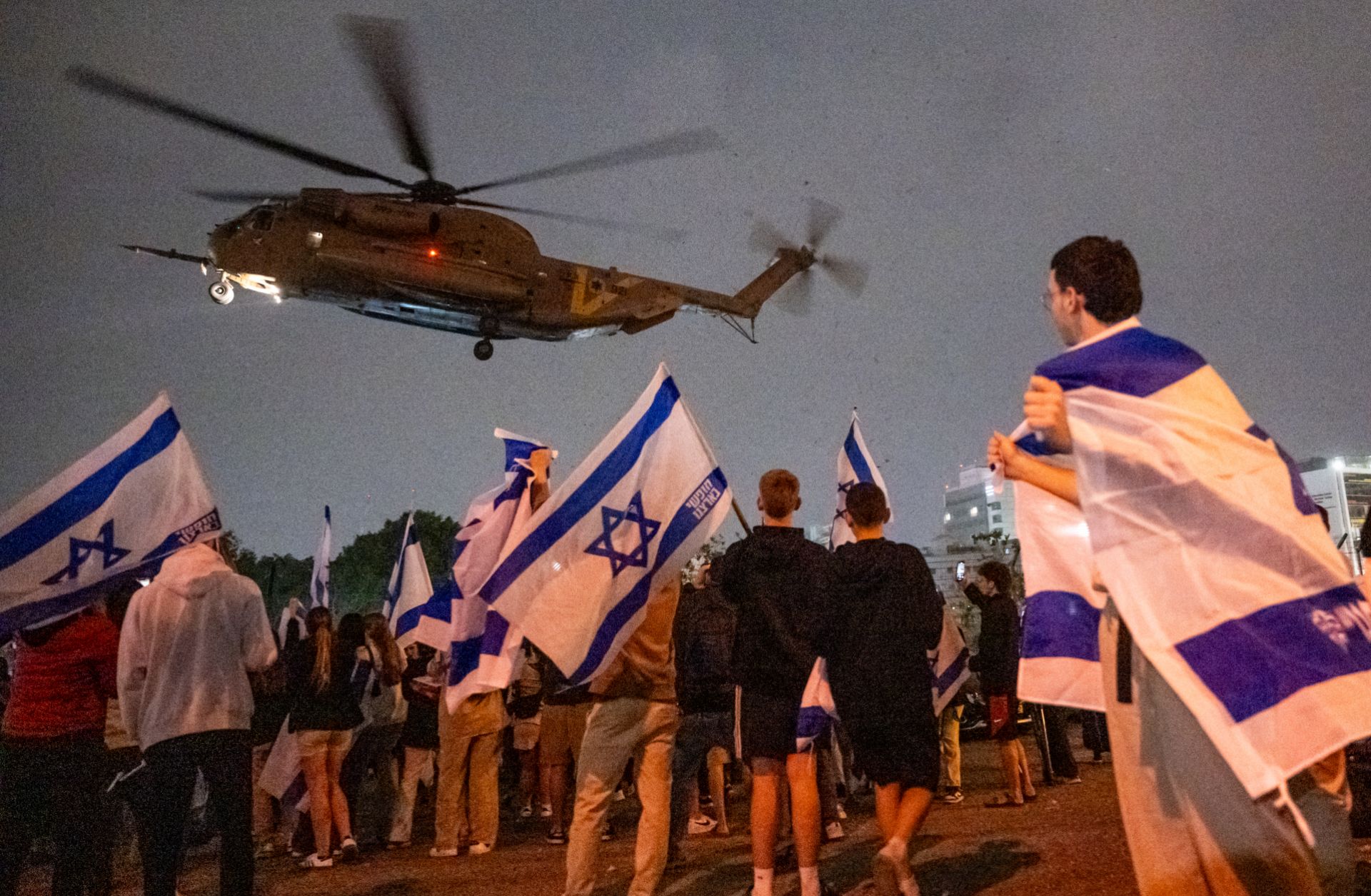 People wave flags and cheer as a helicopter with Israeli hostages released earlier by Hamas lands at a medical center on Nov. 26, 2023, in Petah Tikva, Israel.