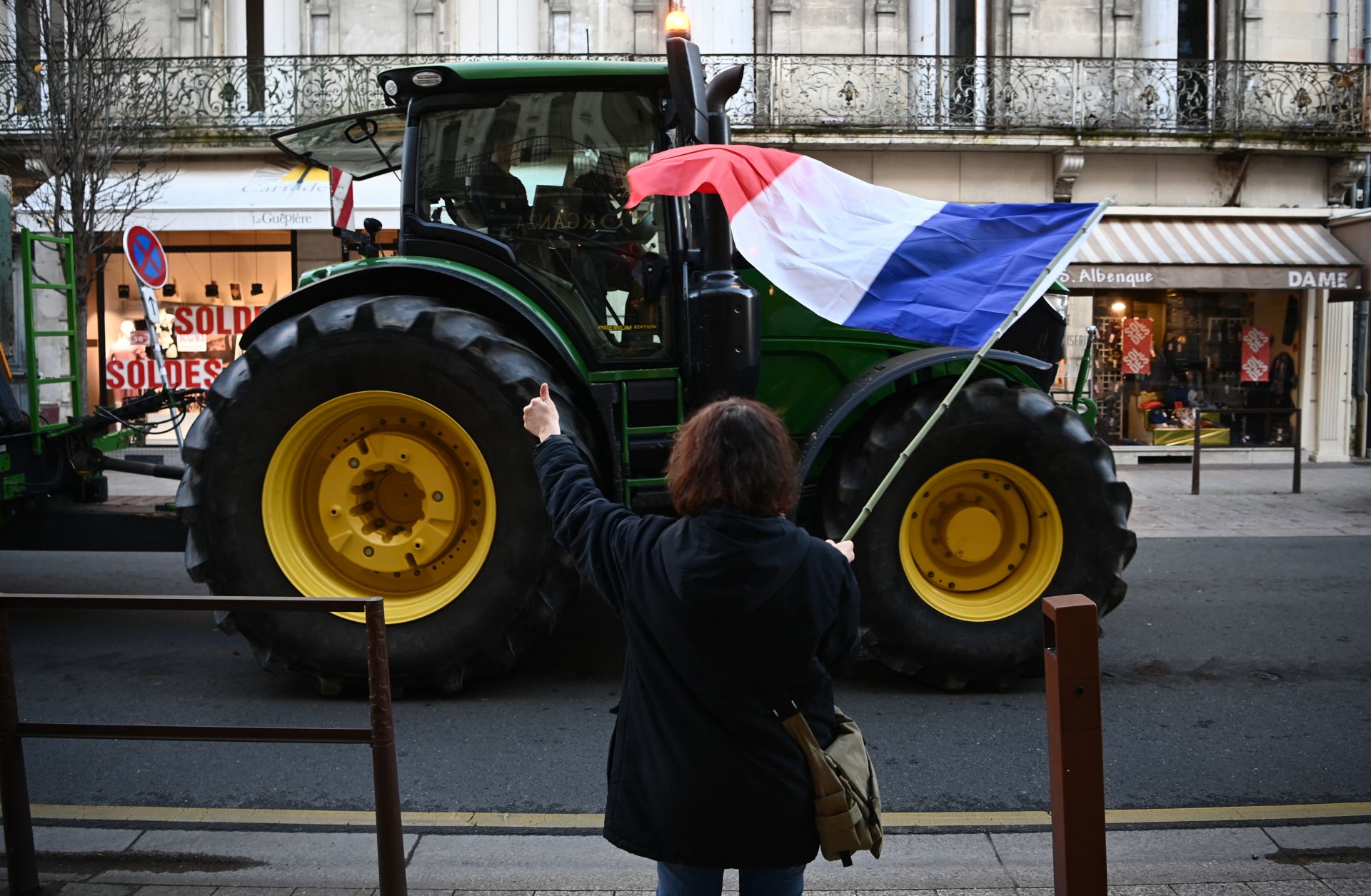A woman waves a French flag in support of protesting farmers as a tractor drives by in Agen, southwerstern France, on Jan. 25, 2024.