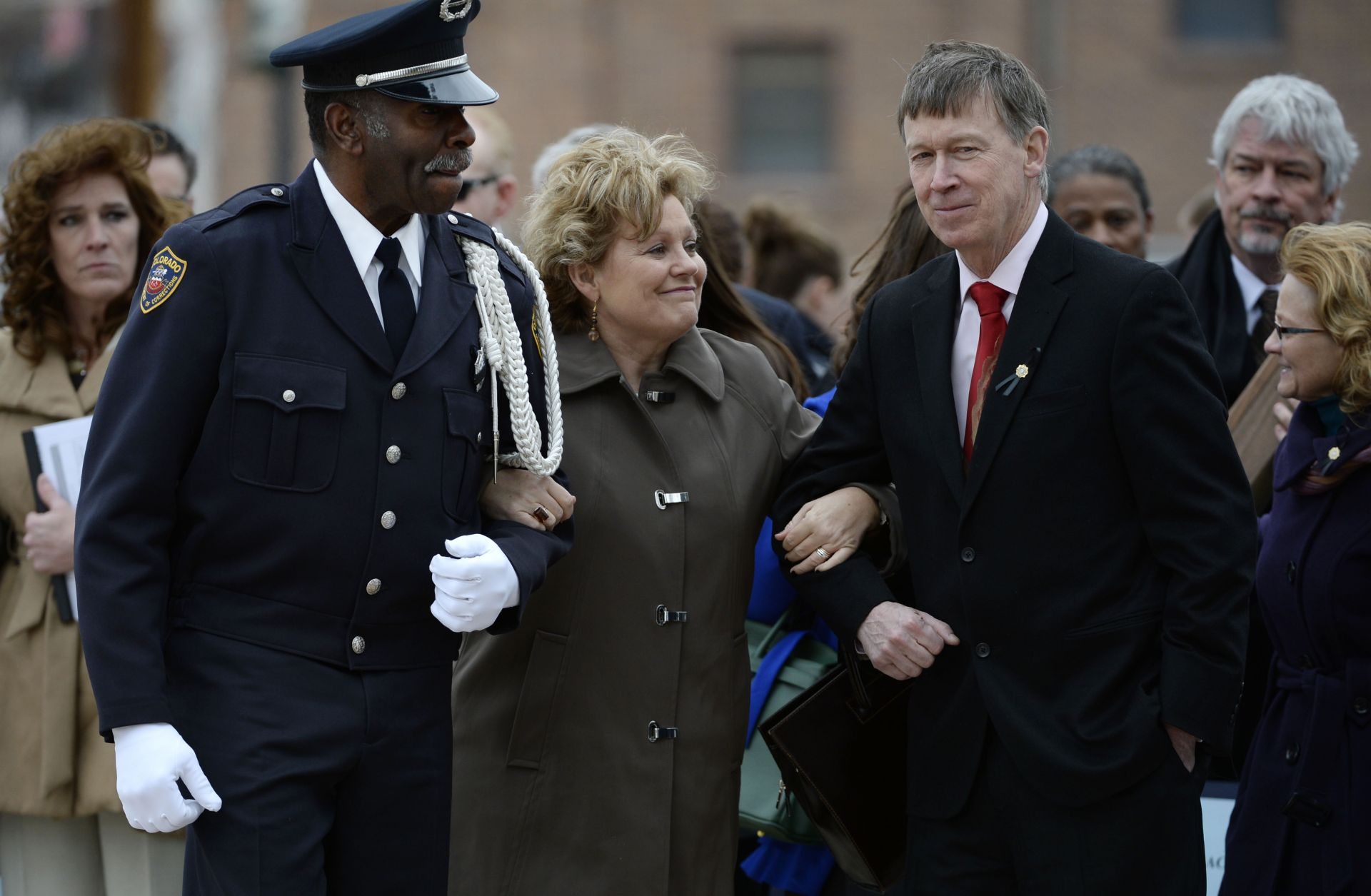 Lisa Clements (C), wife of fallen Department of Correction executive director, Tom Clements, cracks a half-smile as Colorado Department of Corrections Honor Guard member Harry Campbell (L) and Colorado Gov. John Hickenlooper escort her away from a memorial event in Canon City, Colorado, on March 15, 2014.
