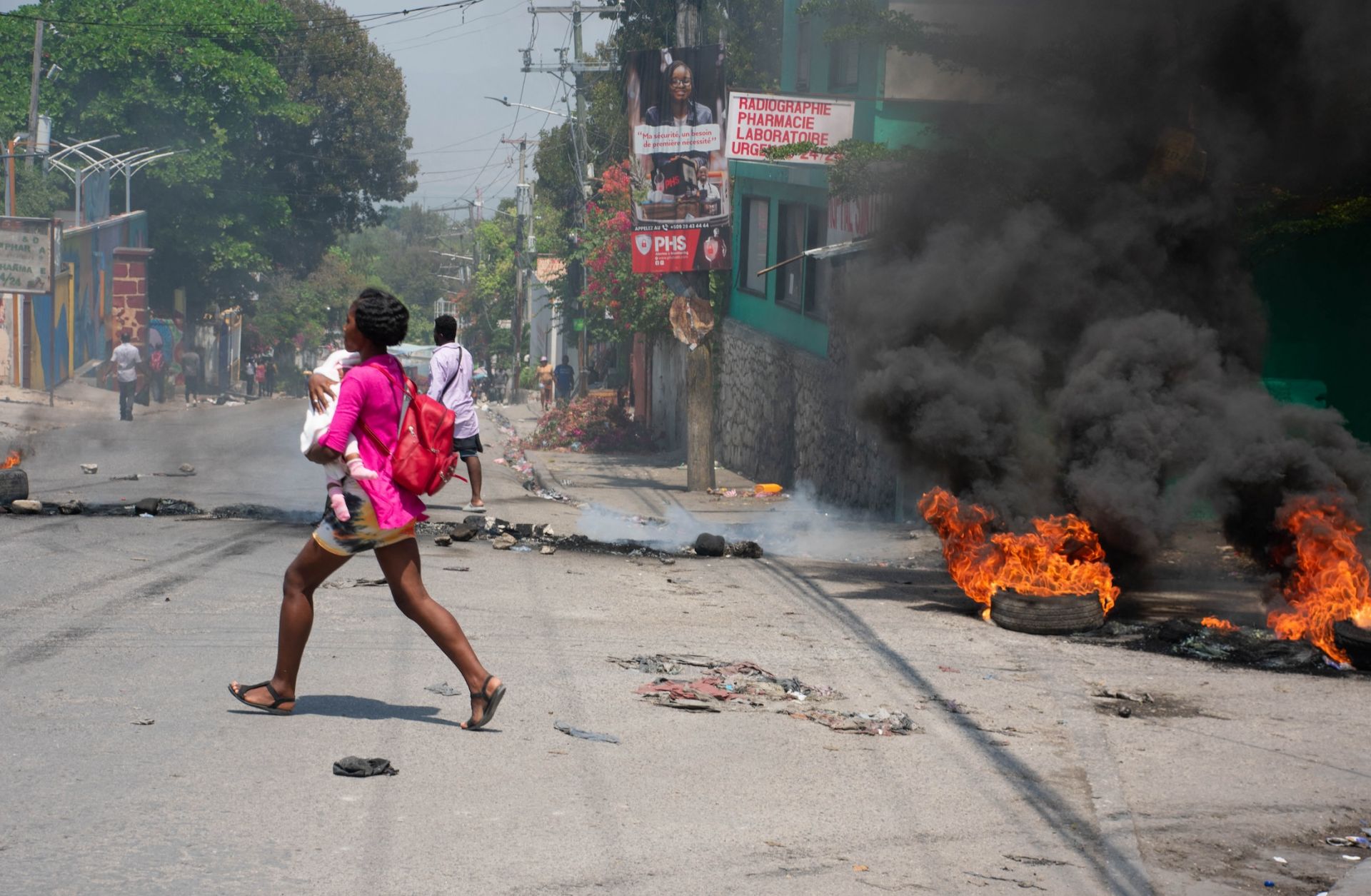 A woman carrying a child runs from an area in Port-au-Prince, Haiti, after hearing gunshots on March 20, 2024.