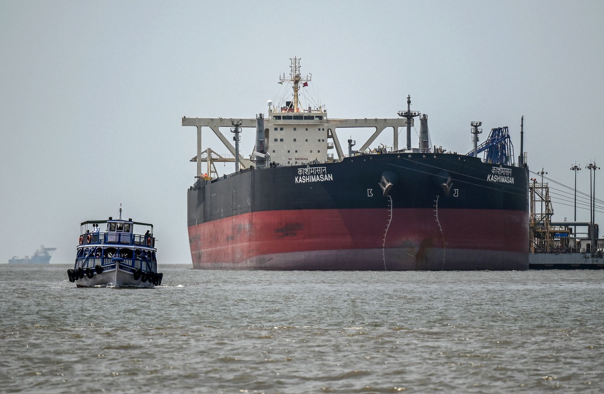 A passenger boat sails past the Indian-flagged oil tanker Kashimasan, which is docked near an offloading terminal at Butcher Island (also known as Jawahar Dweep) off the coast of Mumbai, India, on April 1, 2026.