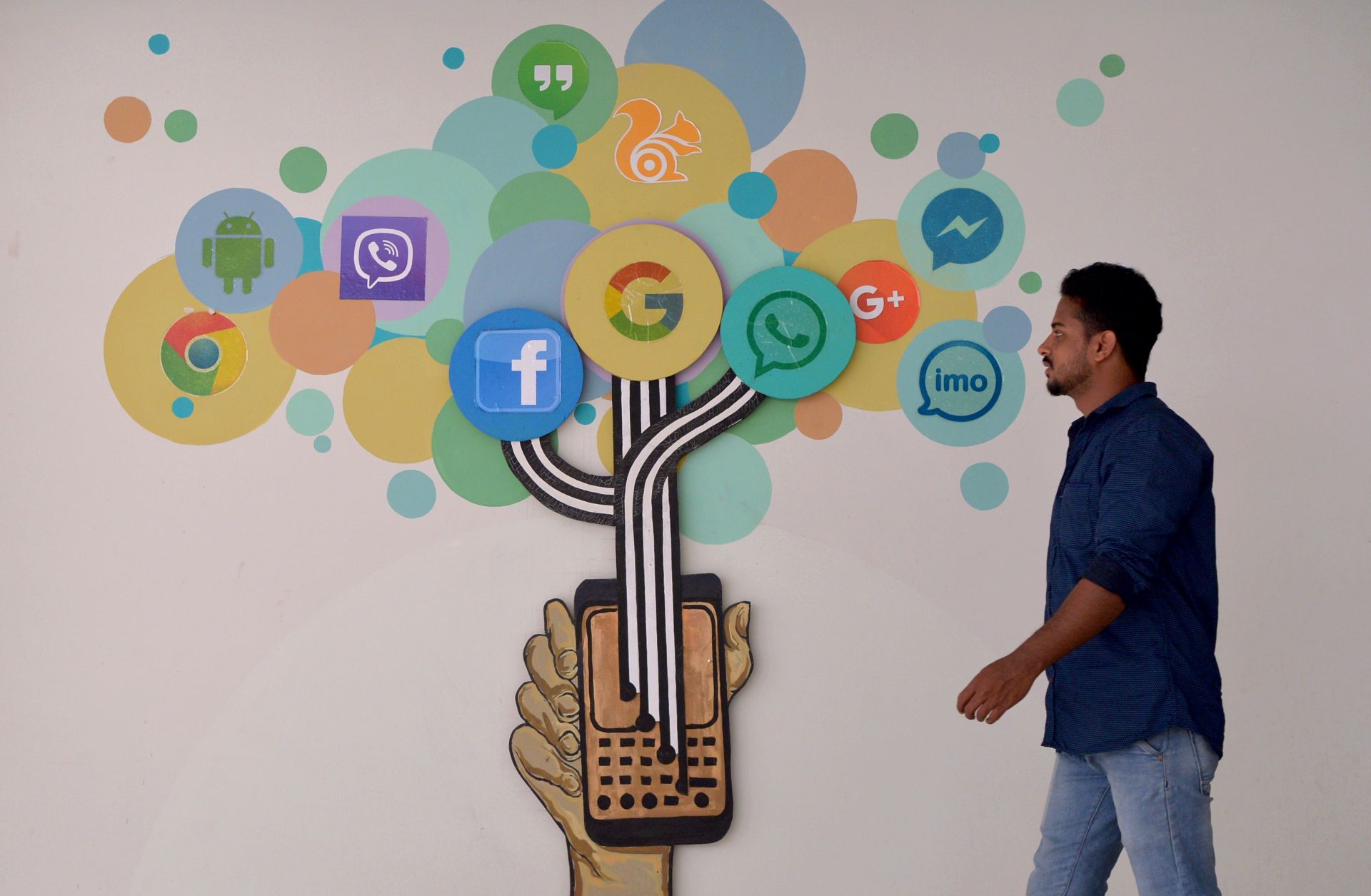A mural of social media logos in a building in Bangalore. An Indian visitor walks past a mural of social media logos in Bangalore.