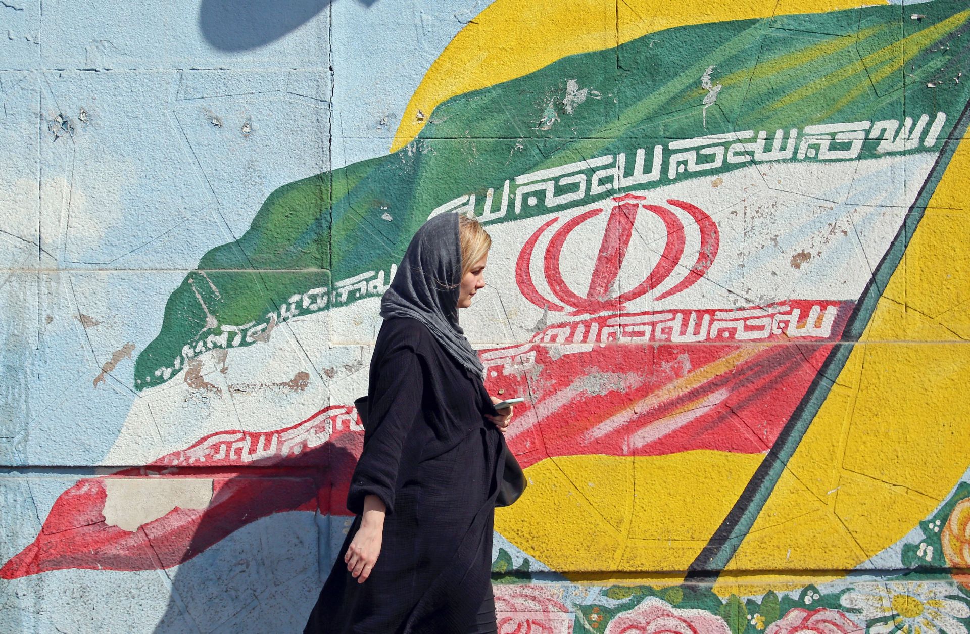 A pedestrian walks past a mural depicting the Iranian national flag in Tehran, Iran. 