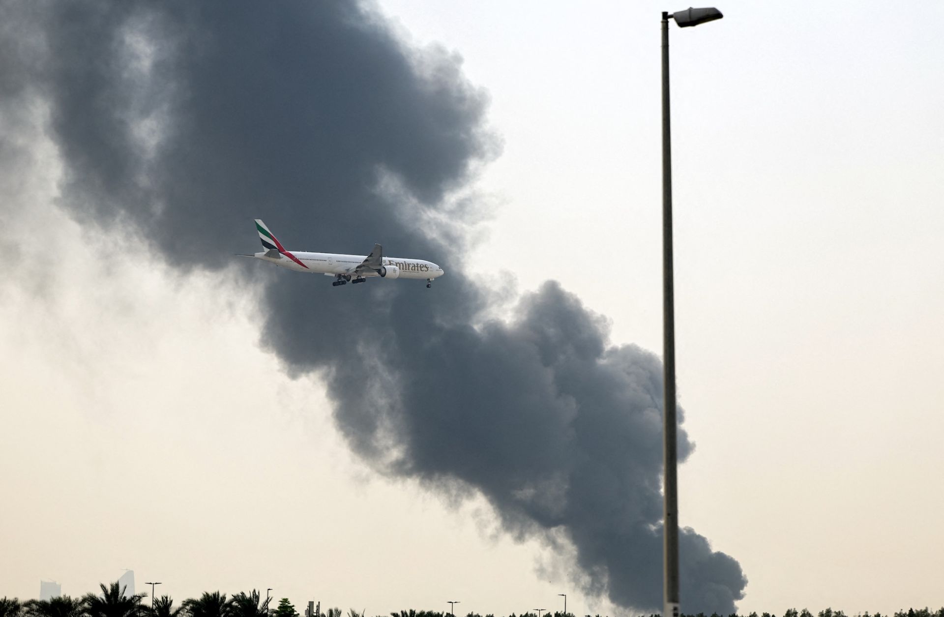 An Emirates Boeing 777 aircraft prepares for landing as a smoke plume rises from an ongoing fire near Dubai International Airport in Dubai on March 16.