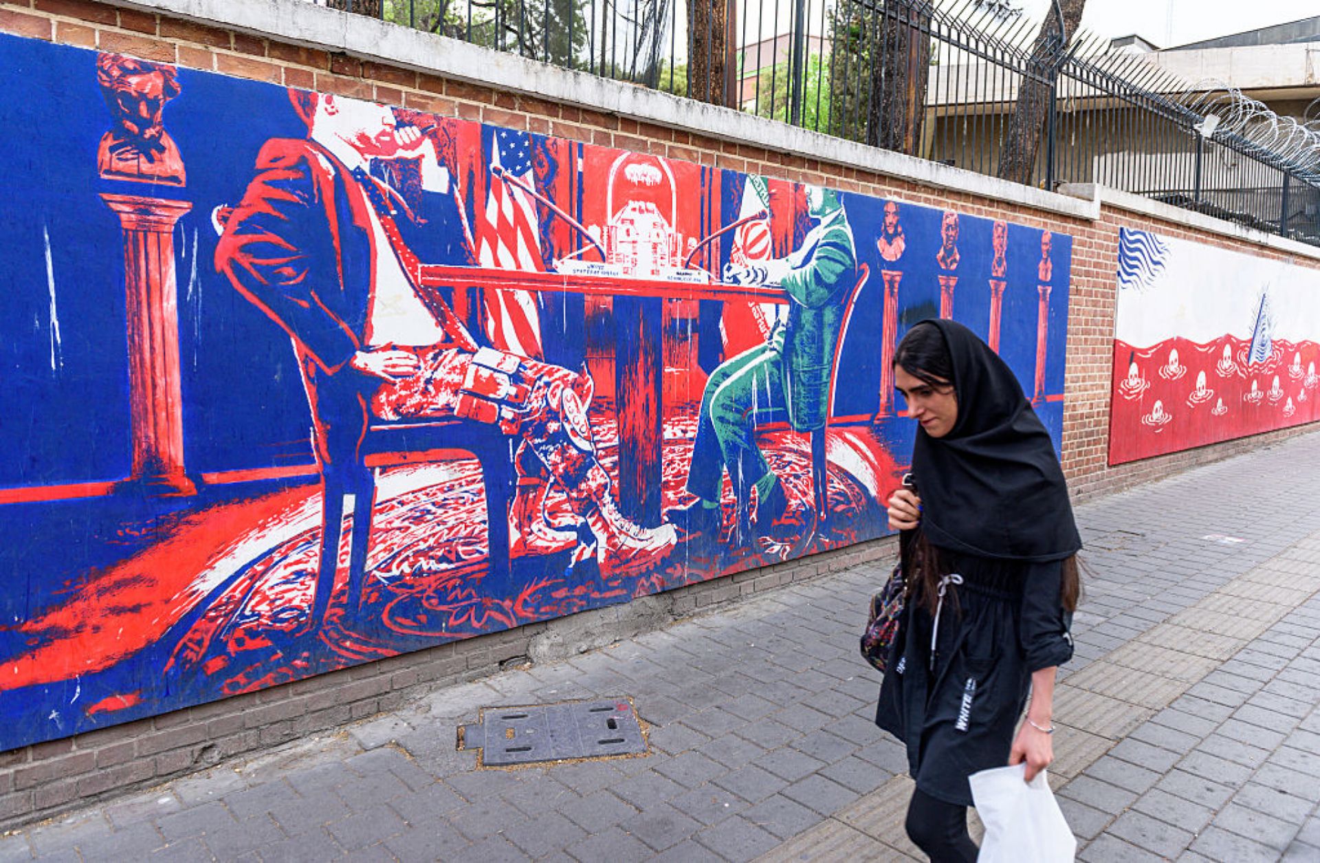 A woman walks by anti-U.S. murals on the walls of the former U.S. embassy in downtown Tehran, Iran, on April 11, 2025. 