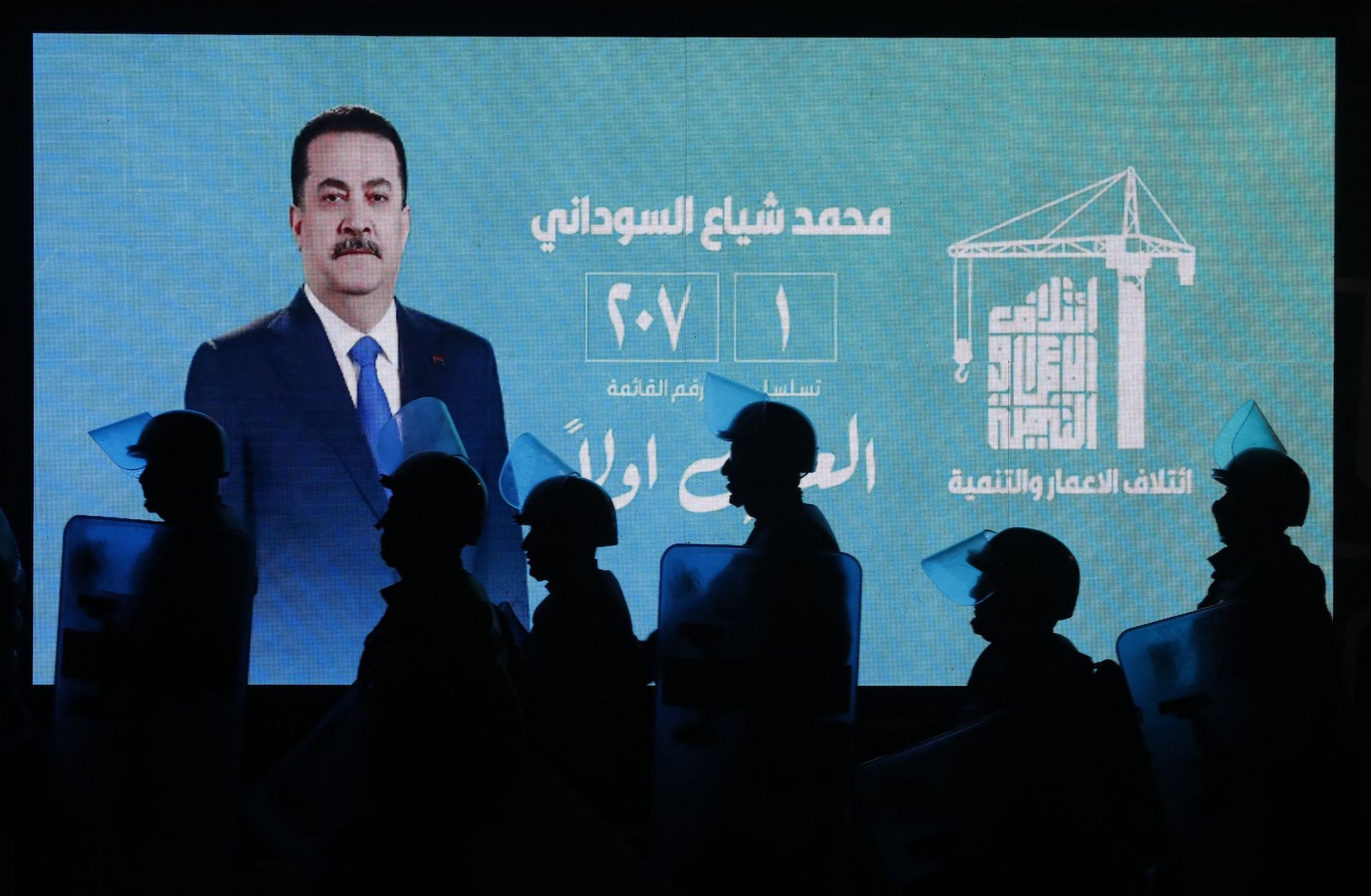 Iraqi riot police walk past a screen displaying a portrait of incumbent Iraqi Prime Minister Mohammed Shia al-Sudani during celebrations by his supporters following the announcement of preliminary election results in Baghdad on Nov. 12, 2025. 