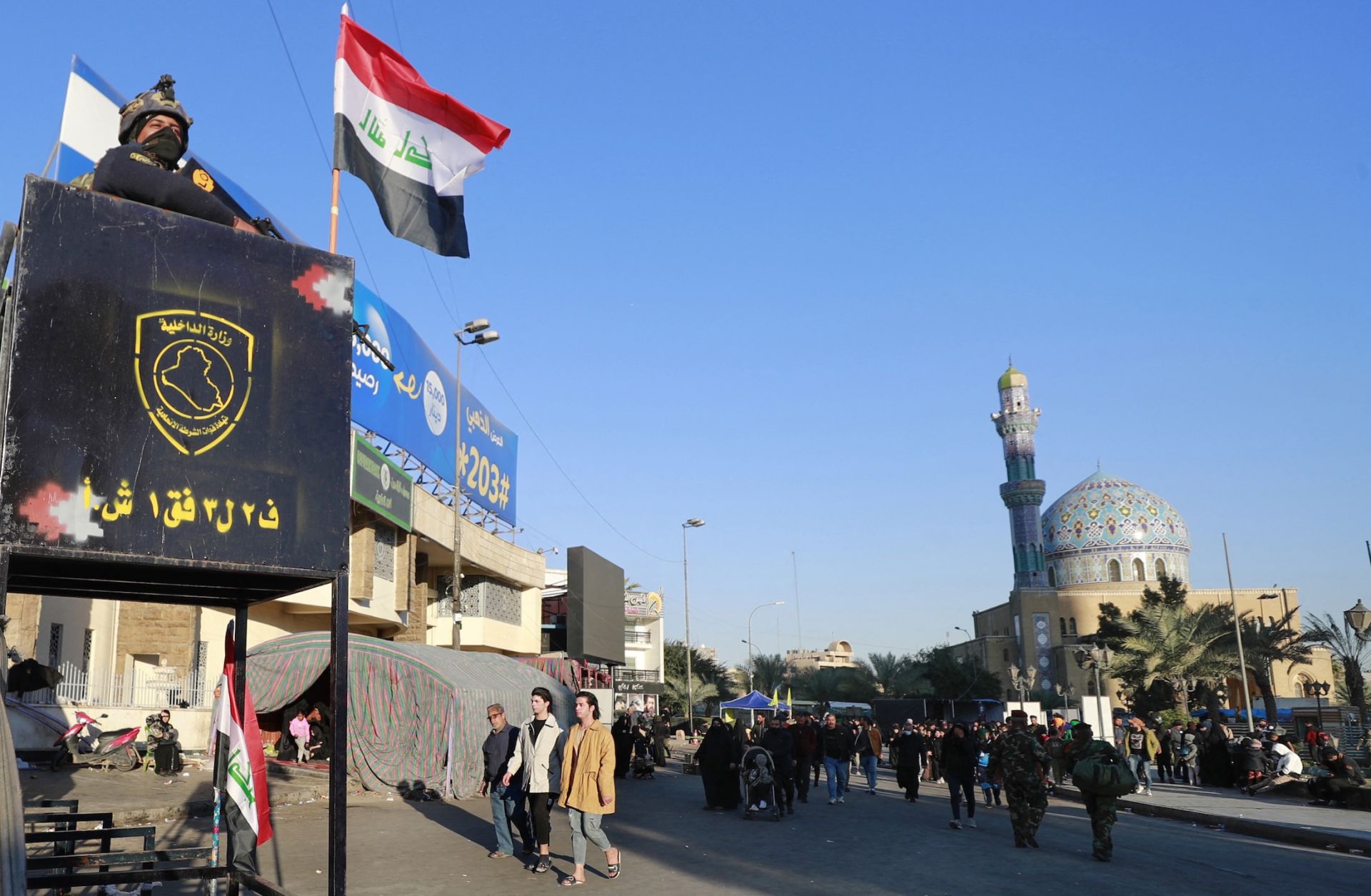 A member of the Iraqi security forces stands guard next to a national flag as pilgrims march from the center of Baghdad toward the shrine of Imam Moussa al-Kadhim, the seventh of 12 revered imams in Shiite Islam, during an annual religious commemoration on Feb. 16, 2023.
