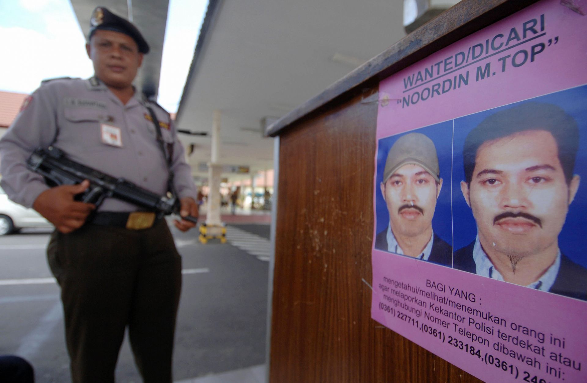 A policeman next to a poster of Noordin Mohammed Top on Aug. 8, 2009, at Bali's Denpasar airport.