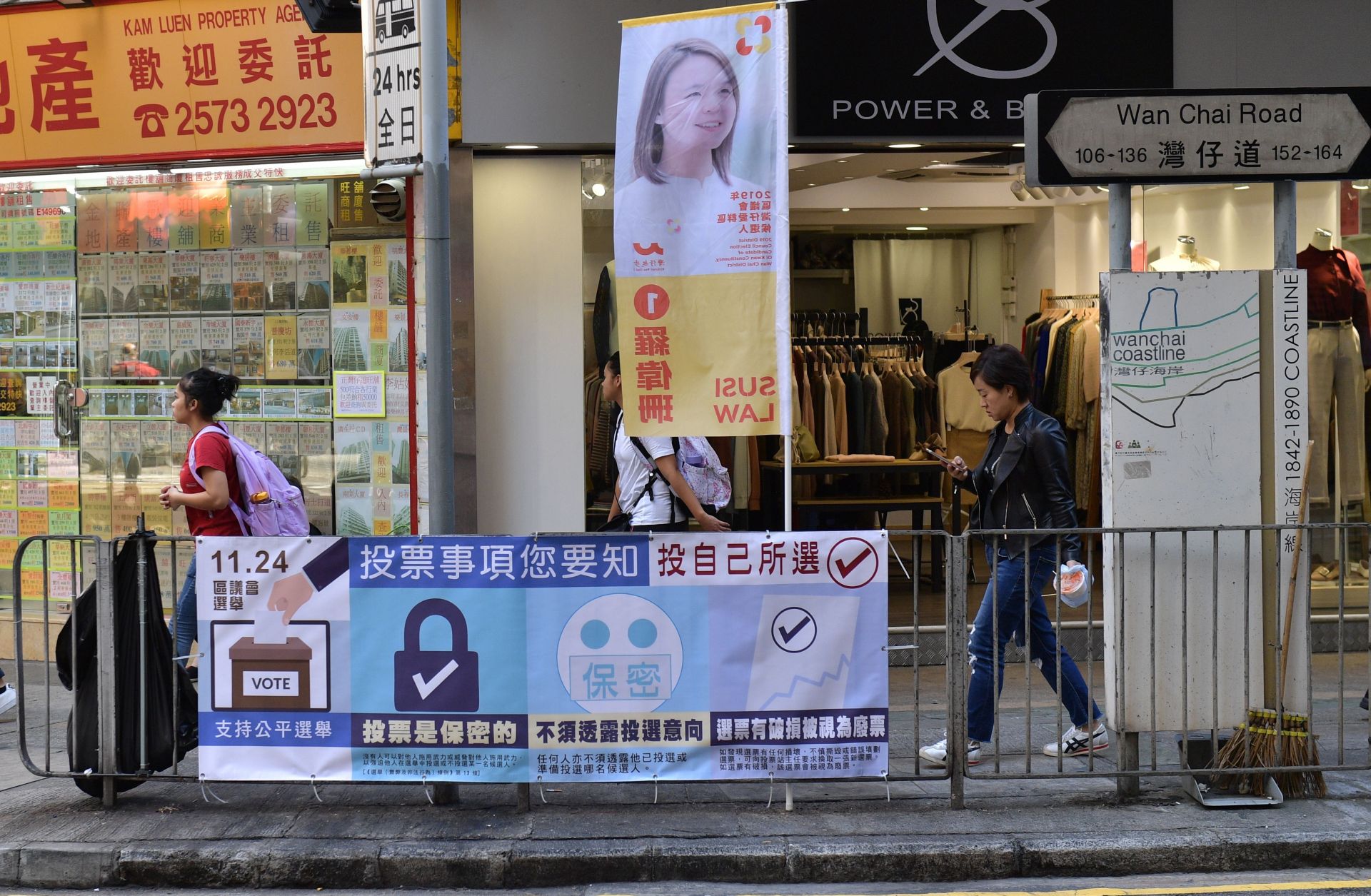 This Nov. 22, 2019, photo shows pedestrians walking past a banner for Hong Kong's district council elections, which are scheduled to take place Nov. 24.