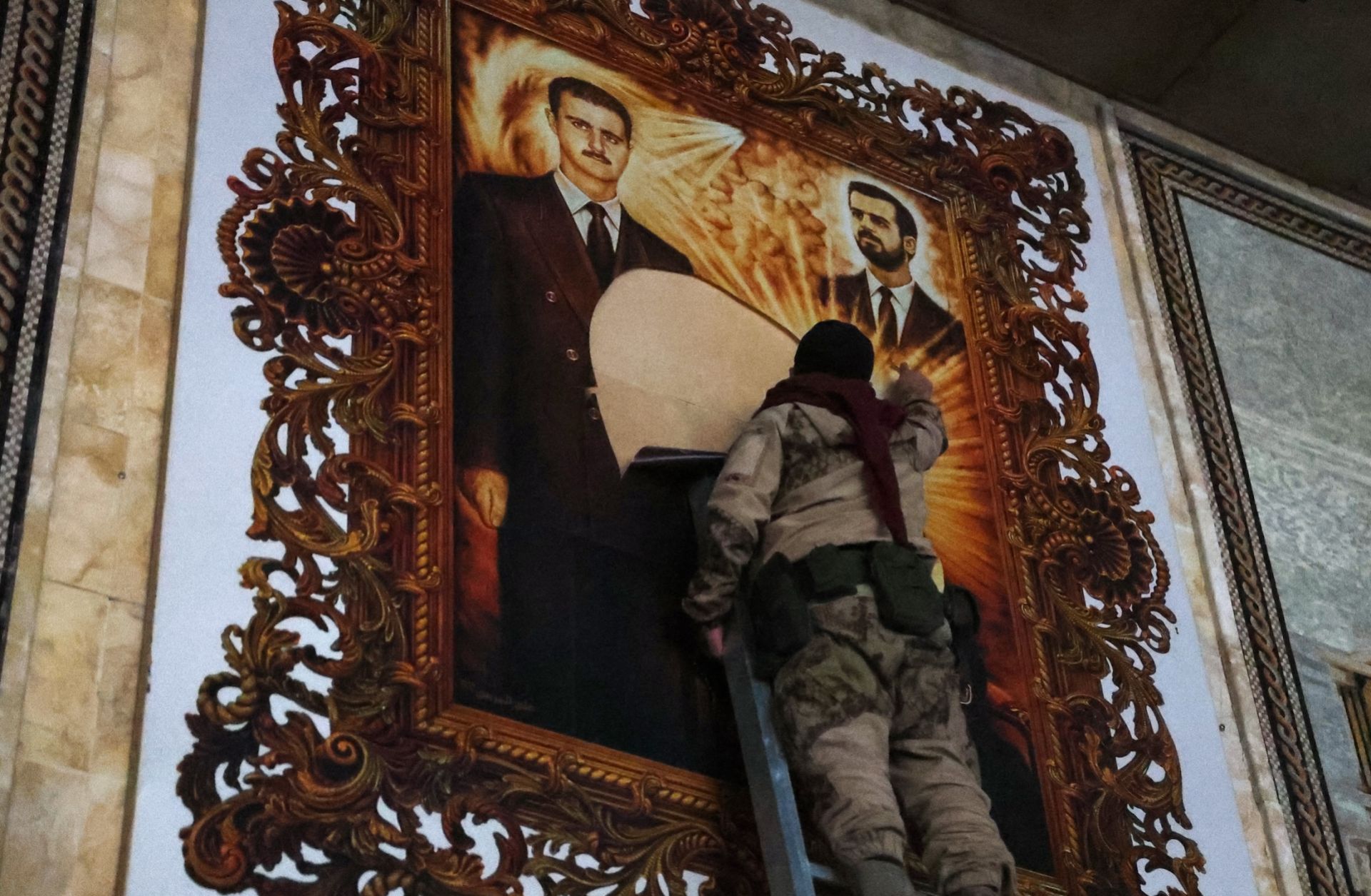 An anti-regime fighter tears off a poster depicting Syrian President Bashar al Assad (left) and his brother Maher at the airport in the northern Syrian city of Aleppo on Dec. 2, 2024. 