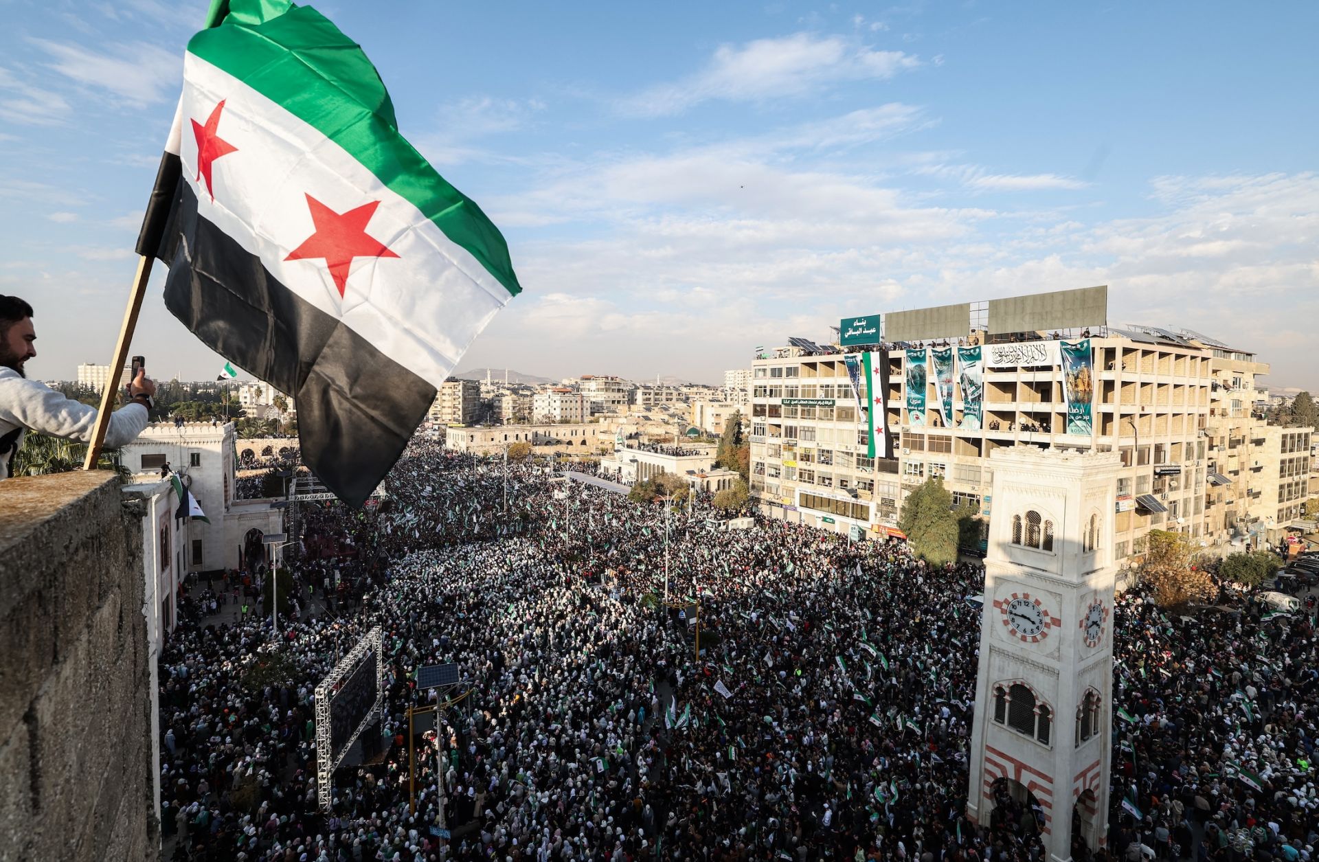 A Syrian flag flutters above crowds gathering in central Hama, Syria, during celebrations on Dec. 5, 2025, marking one year since the fall of former President Bashar al Assad's regime.
