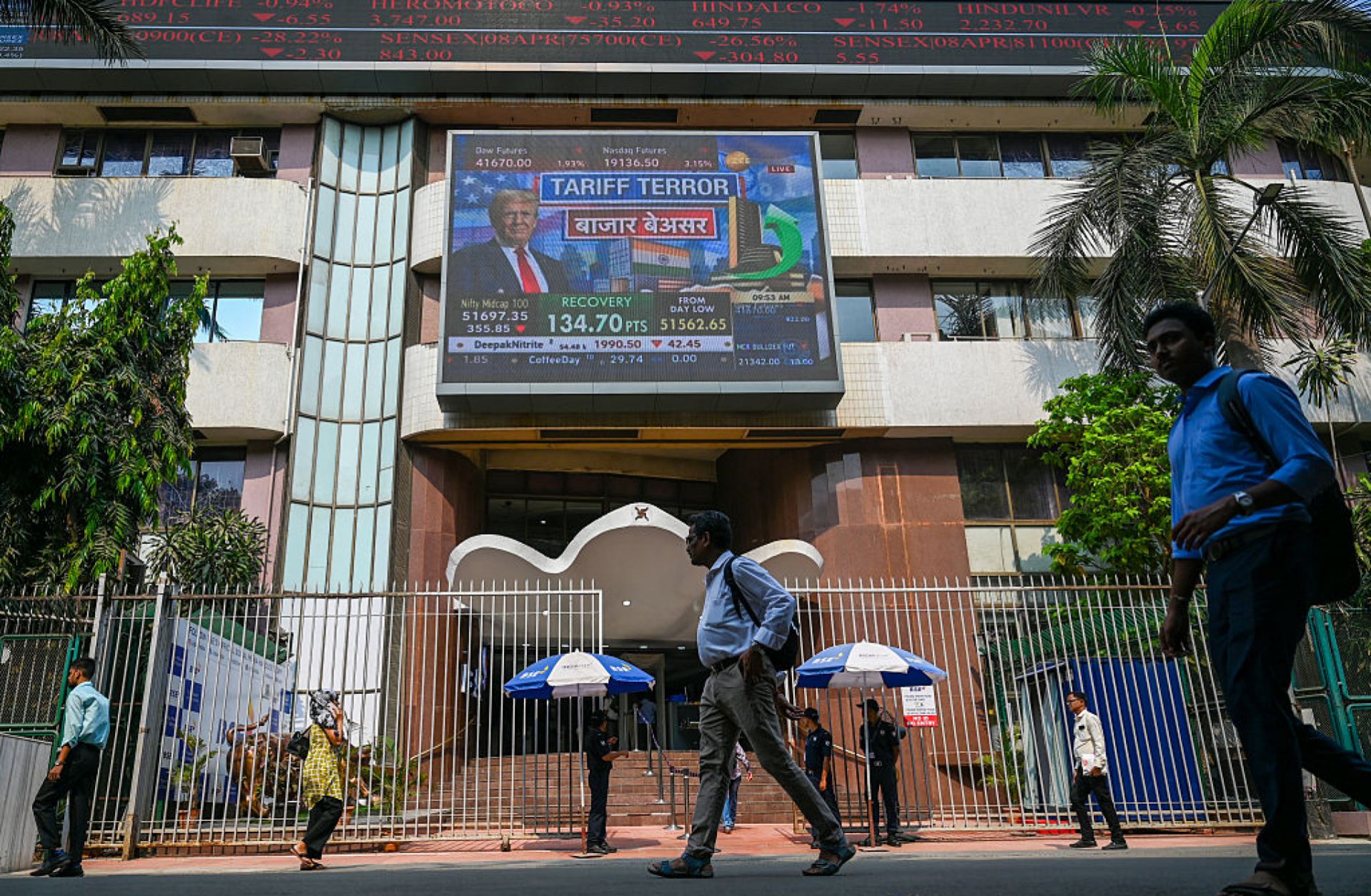 Pedestrians walk past a broadcast screen of the Bombay Stock Exchange (BSE) in Mumbai on April 3, 2025, airing news of U.S. President Donald Trump unveiling sweeping new trade tariffs. 