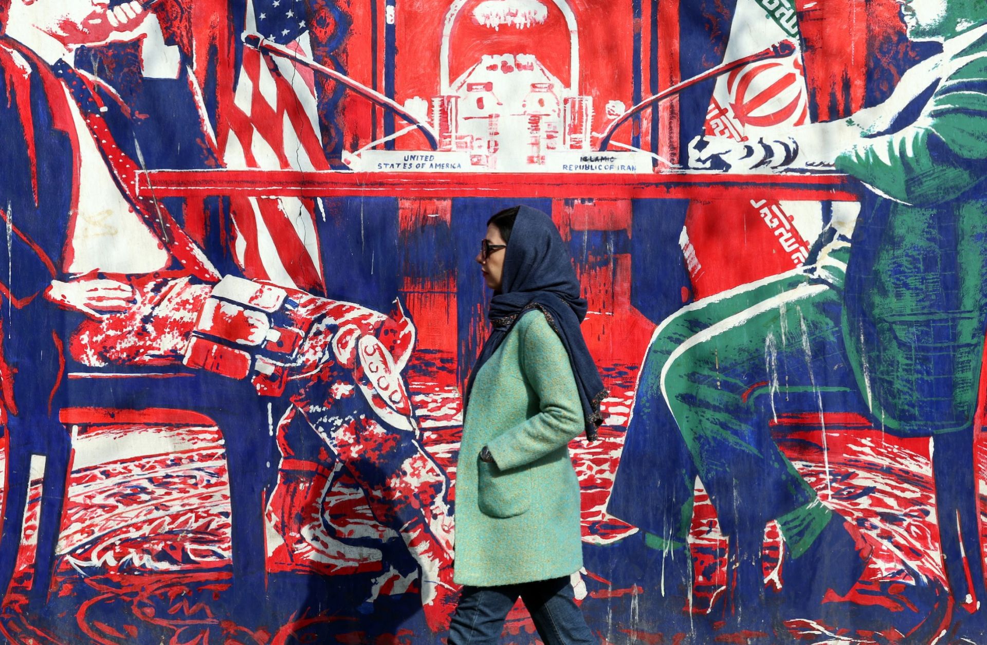 An Iranian woman walks past a mural depicting Iran and the United States at the negotiation table, painted on the outer walls of the former U.S. embassy in Tehran, on Feb. 6, 2026.