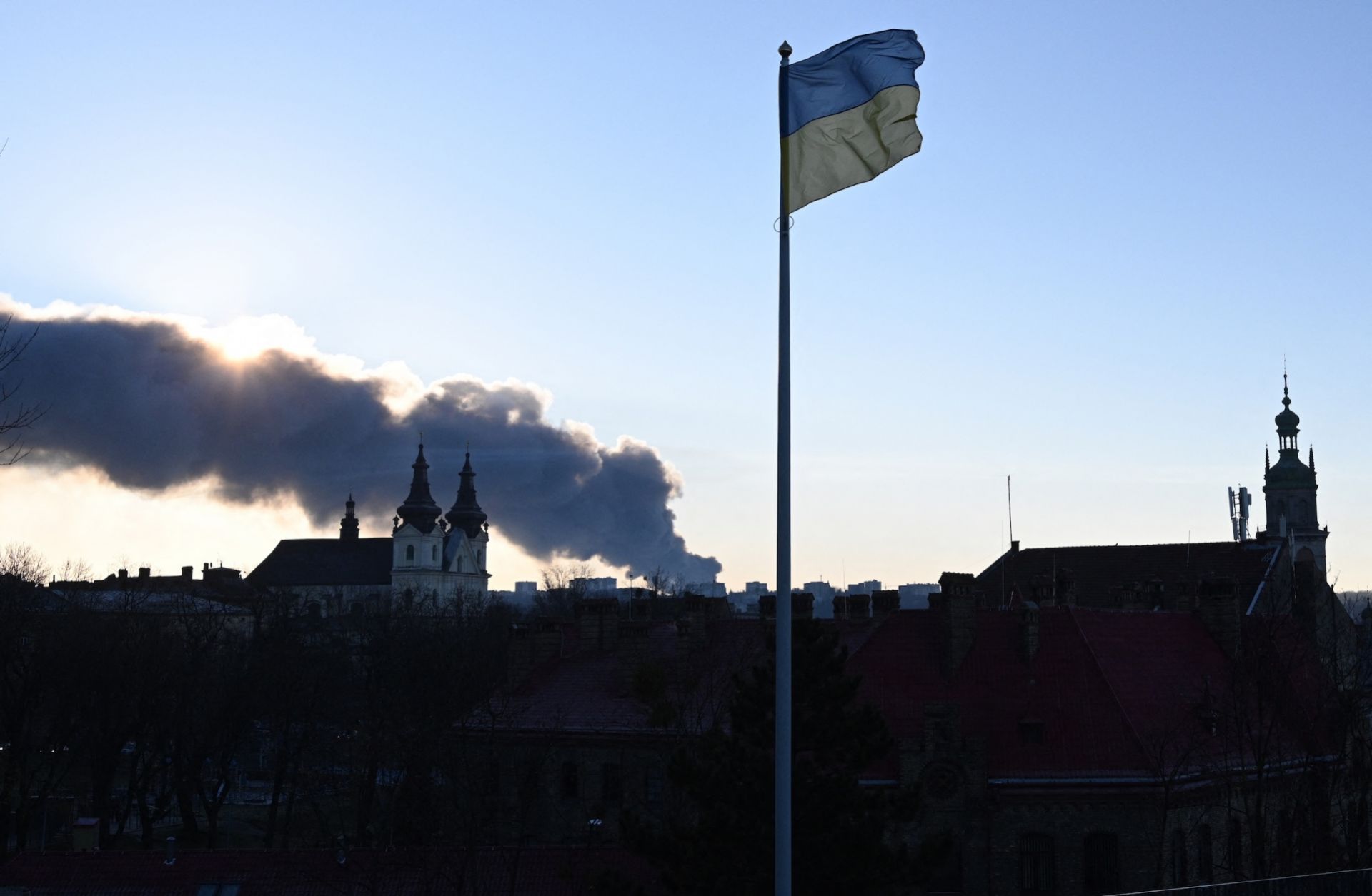 Smoke rises in the background as a Ukrainian flag flutters in the wind following a mass overnight Russian drone and missile attacks, in the western Ukrainian city of Lviv on Nov. 19, 2025. 