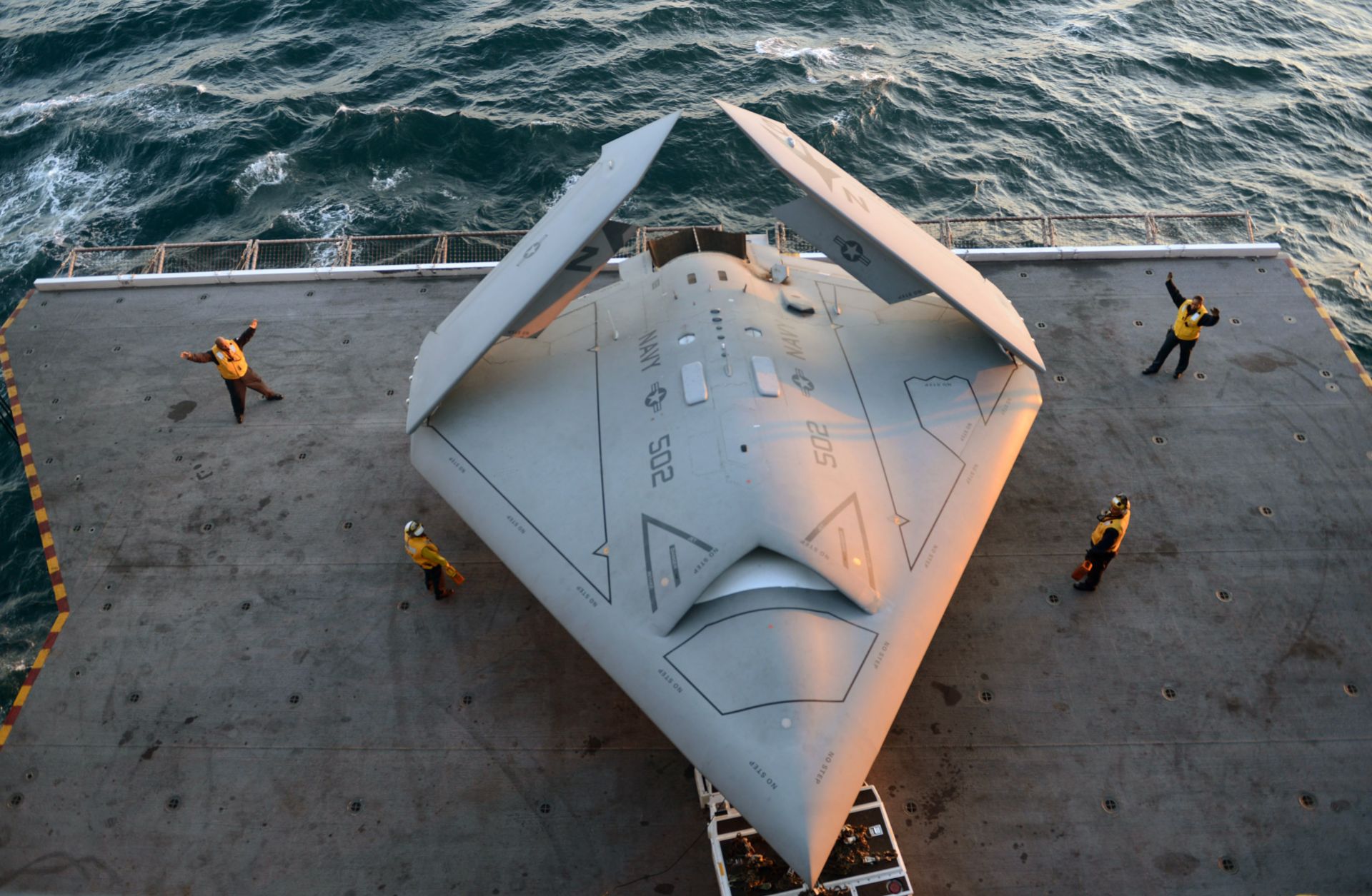 A picture showing U.S. sailors move an X-47B Unmanned Combat Air System (UCAS) demonstrator onto an aircraft elevator aboard the aircraft carrier USS George H.W. Bush.