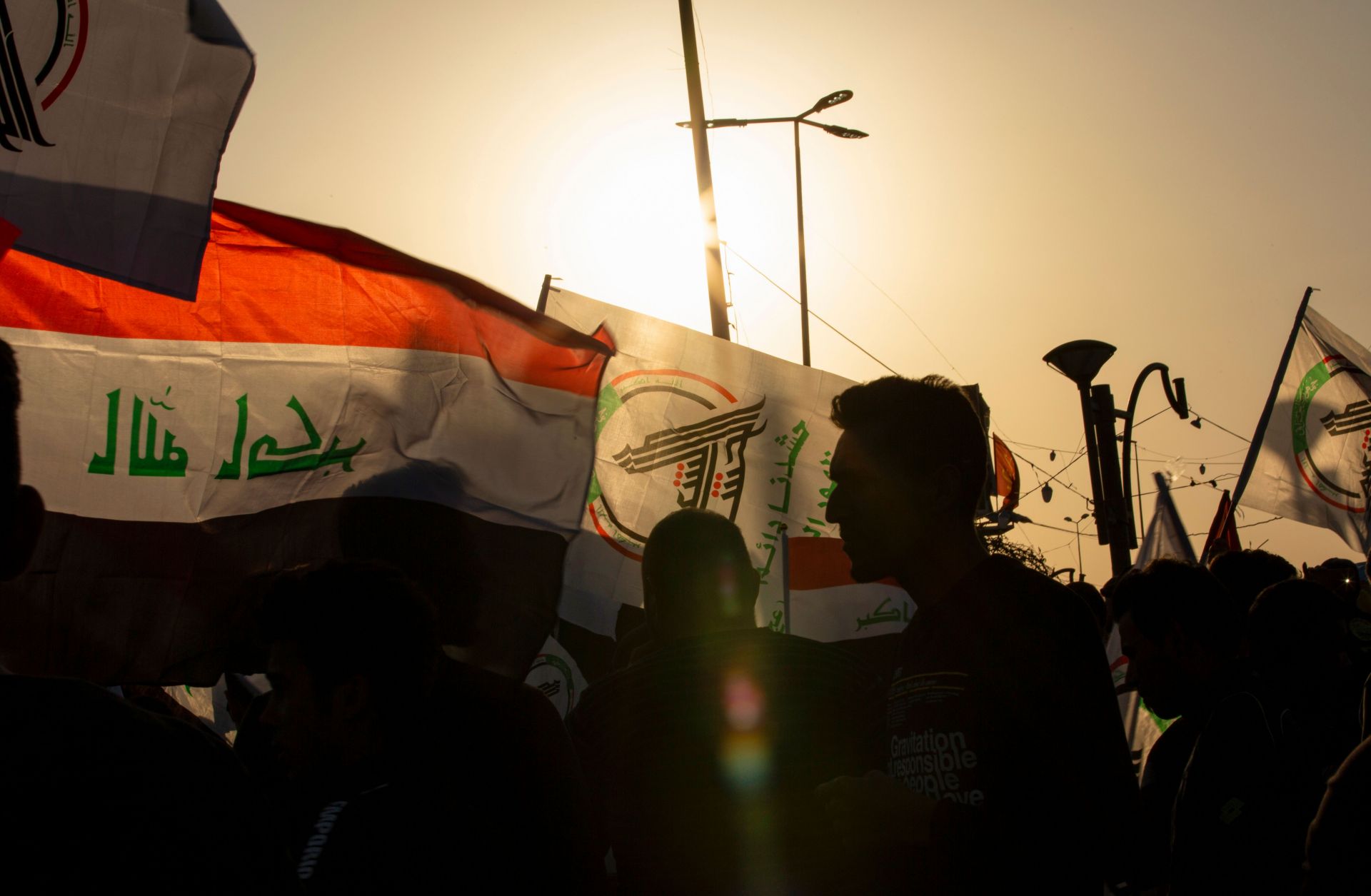 Protesters waving the Iraqi flag alongside one of an armed network march in Basra to denounce U.S. airstrikes that killed dozens of Iraqi militia members.