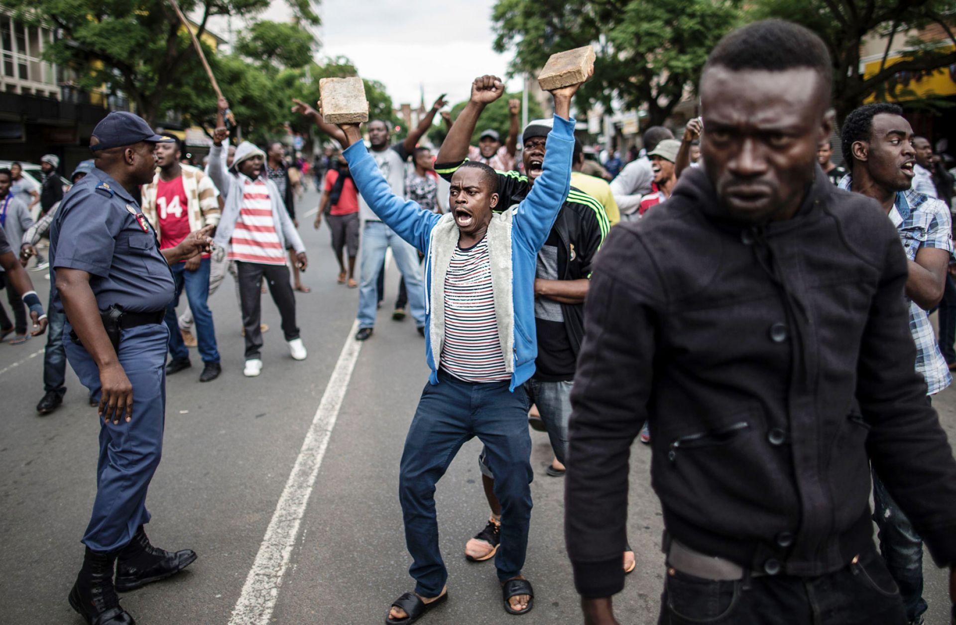 A crowd of Nigerians faces off with South Africans in Pretoria on Feb. 24 while a South African policeman (L) tries to calm them. Populism has taken root in the impoverished and unemployed segments of South African society.
