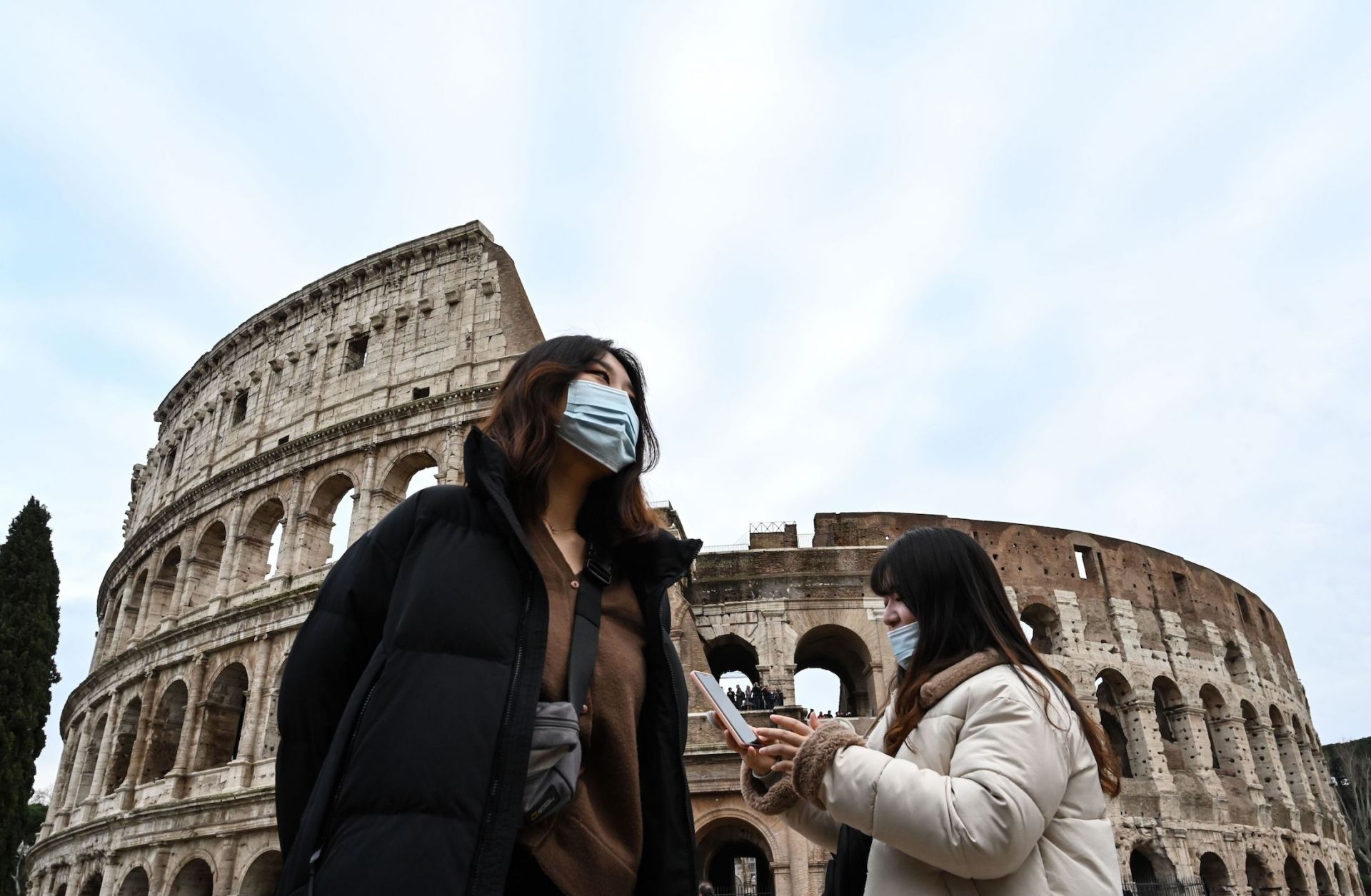 Two women wearing blue, protective respiratory masks take a tour outside the Colosseum in Rome, Italy, on Jan. 31, 2020, after two cases of the new coronavirus were confirmed in the city. 