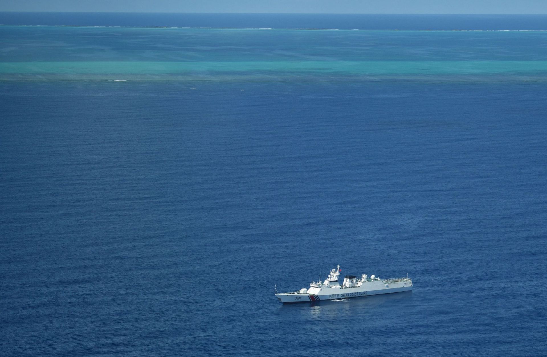 A photo taken during a Philippine surveillance flight on Sept. 28, 2023, shows a Chinese coast guard ship on patrol near the Scarborough Shoal (seen in the background) in the South China Sea.