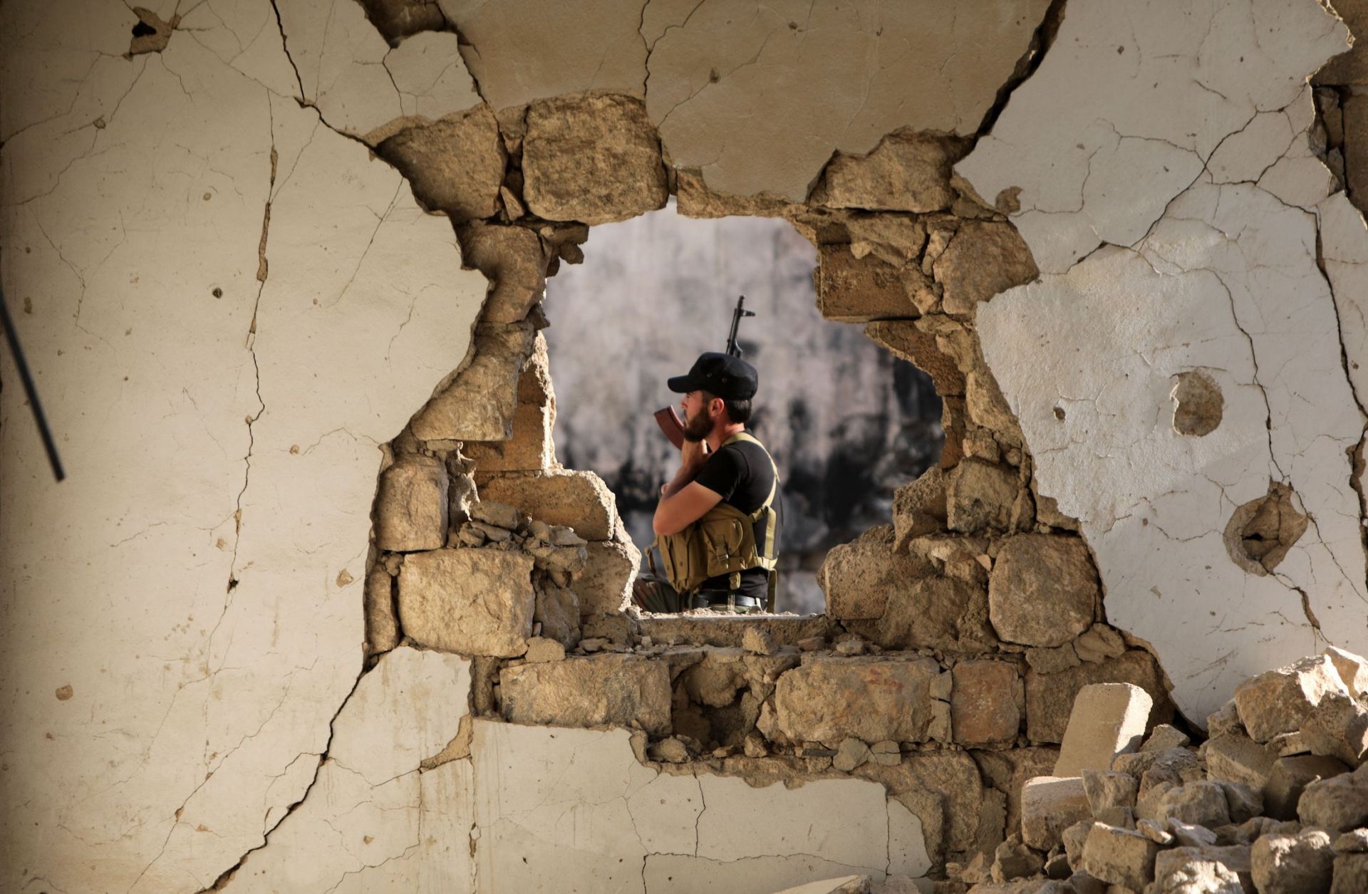 A fighter of the Turkish-backed Syrian National Army is seen through the hole of a damaged building in the northern town of Marea, facing the Kurdish-controlled area of Tal Rifaat, on Aug. 2, 2022. 