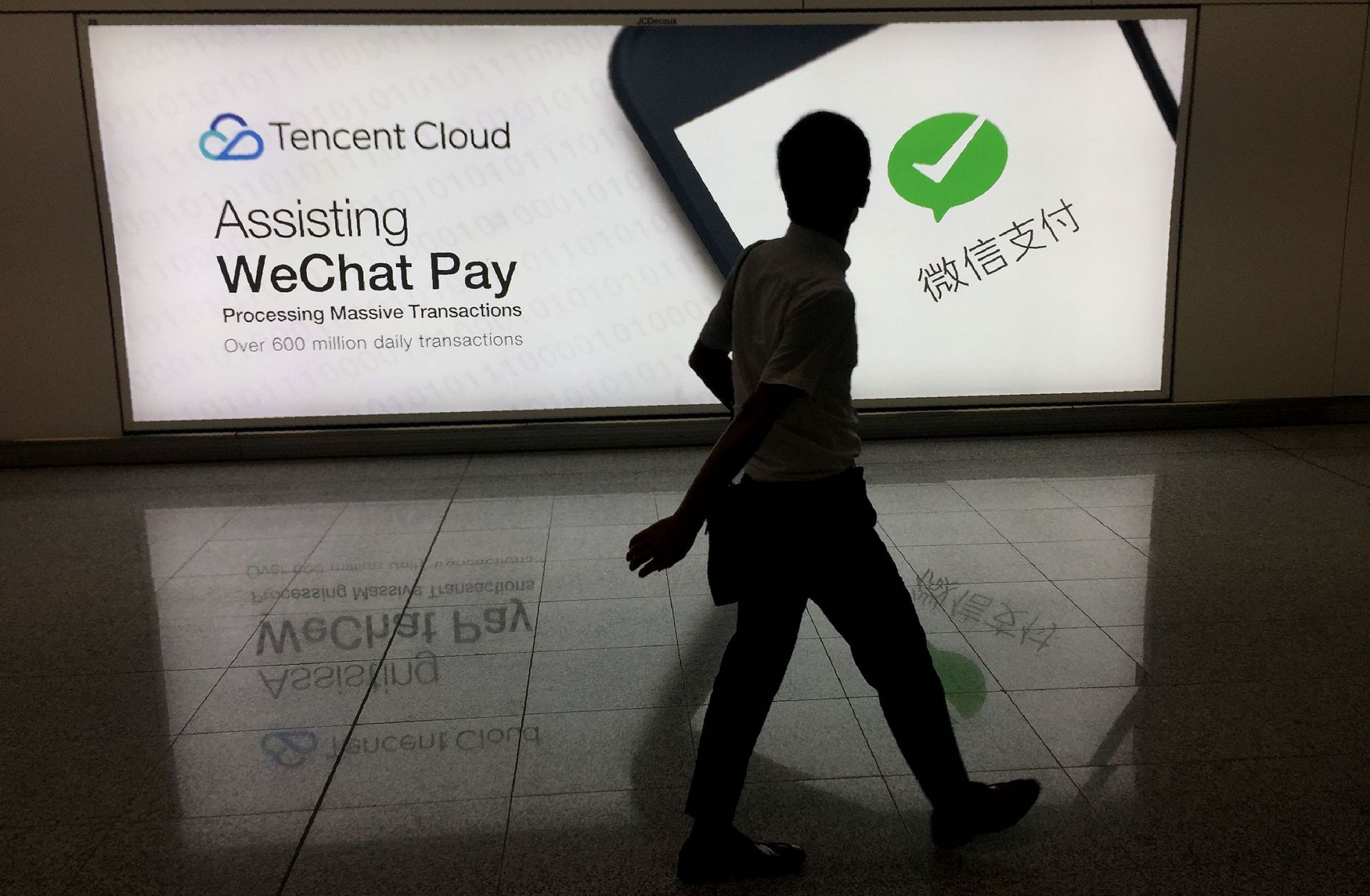 In this August 2017 photo, a man walks past an ad in Hong Kong's international airport for the social media platform WeChat, which is owned by China's Tencent.