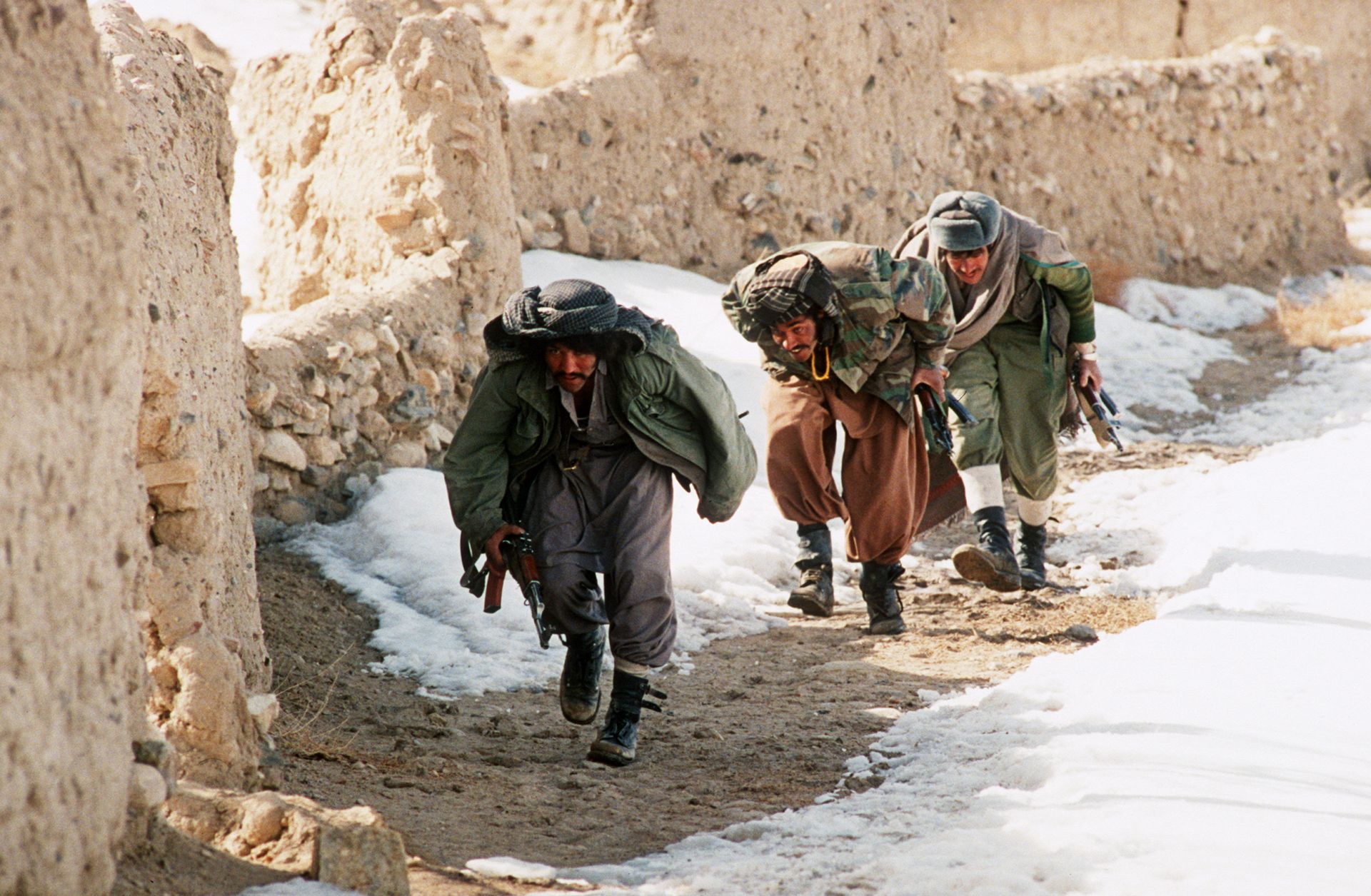 A group of Afghan mujahideen progress behind a wall in the village of Ghazni in southern Afghanistan as they fight Soviet-backed government forces in March 1989. 