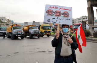 A protester holds a sign as fuel tankers block a road in Lebanon's capital of Beirut during a general strike by public transport and workers unions on Jan. 13, 2022. 