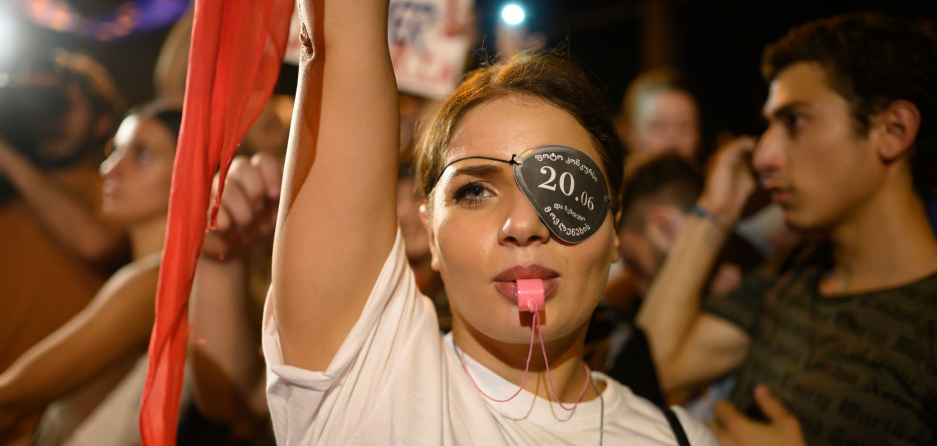 A woman raises her flag and blows a whistle at Georgia's Parliament building. She wears an eye patch to protest the dispersal of a previous demonstration.