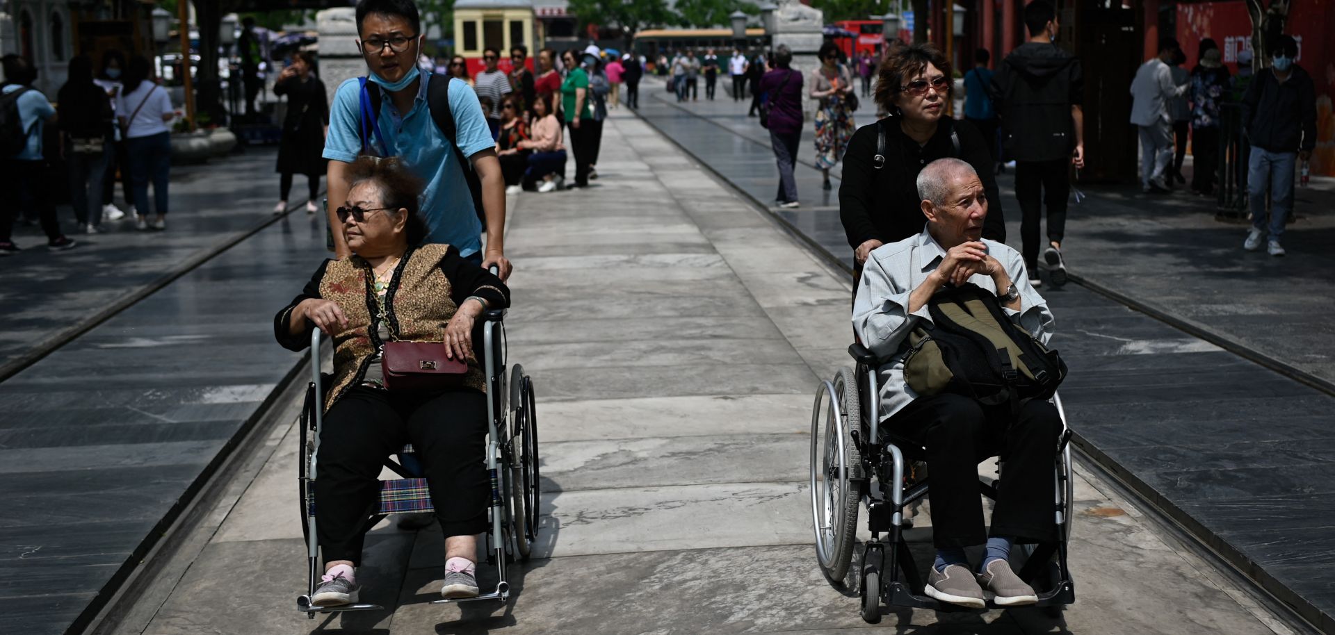 An elderly man and woman are pushed in wheelchairs along a street in Beijing, China, on May 11, 2021.