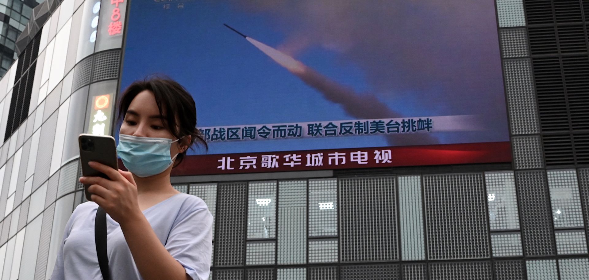 A woman in Beijing uses her mobile phone as she walks in front of a large screen showing a news broadcast about China's military exercises encircling Taiwan on Aug. 4.