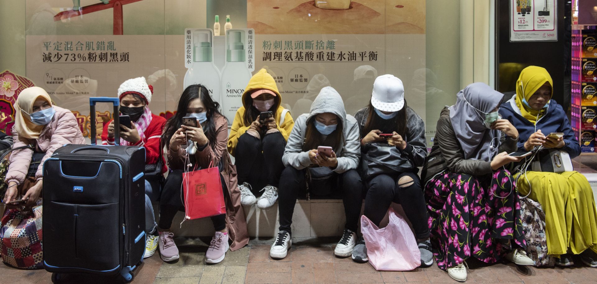 Women sit along the side of a street in Hong Kong on Jan. 28. They’re each wearing sanitary masks to protect themselves from the coronavirus. 