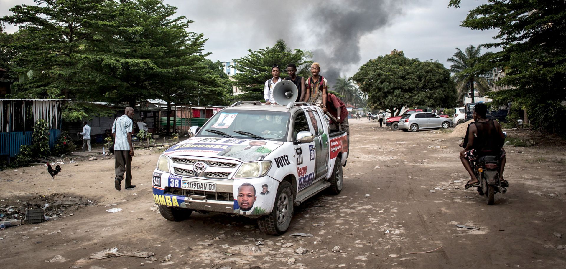 A campaign car is seen as smoke rises from a fire at the independent Congolese electoral commission's warehouse in Kinshasa on Dec. 13, 2018, 10 days ahead of presidential elections that have been foreshadowed by violence.