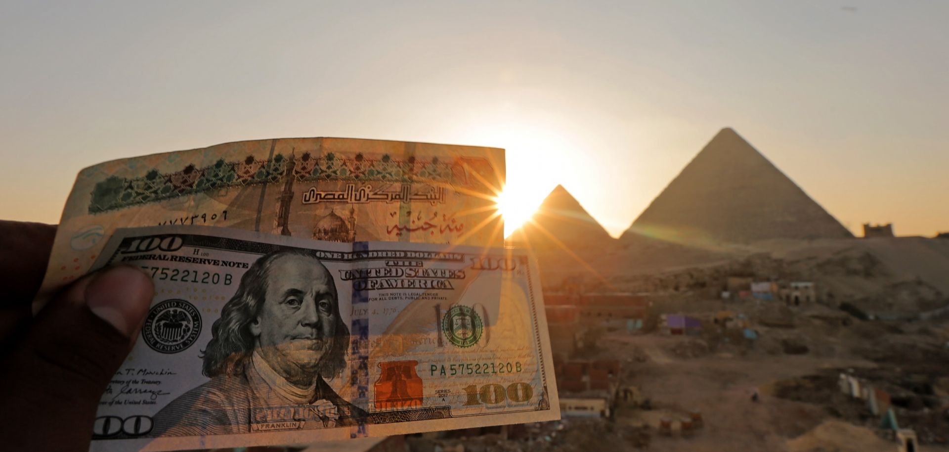 A 100-pound Egyptian banknote is held next to a $100 U.S. banknote near the Great Pyramids at Giza on Jan. 17, 2023.