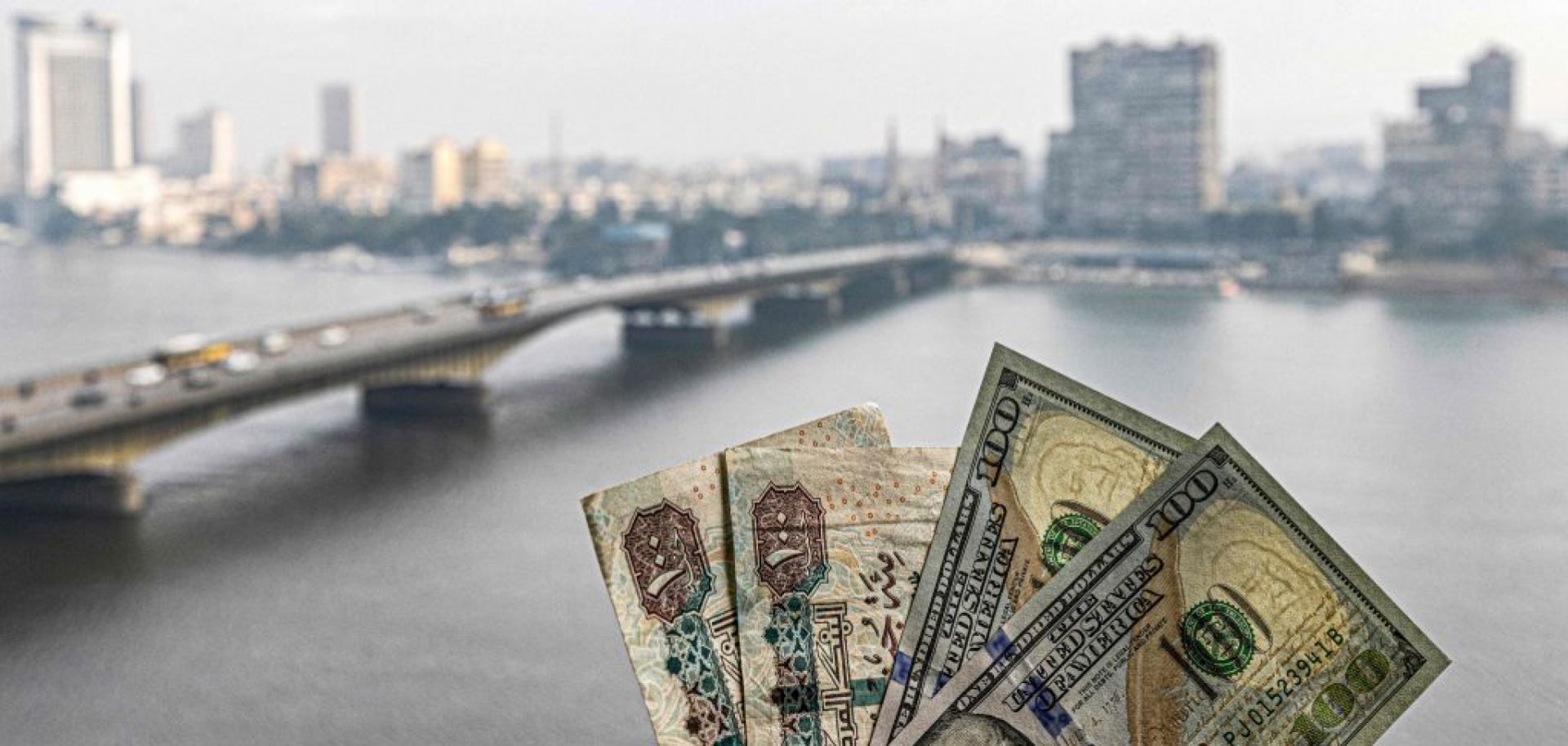 Two pairs of U.S. hundred dollar bills and Egyptian hundred pound notes are held before a window showing the skyline of Egypt's capital Cairo and the Nile River on Jan. 16, 2023.